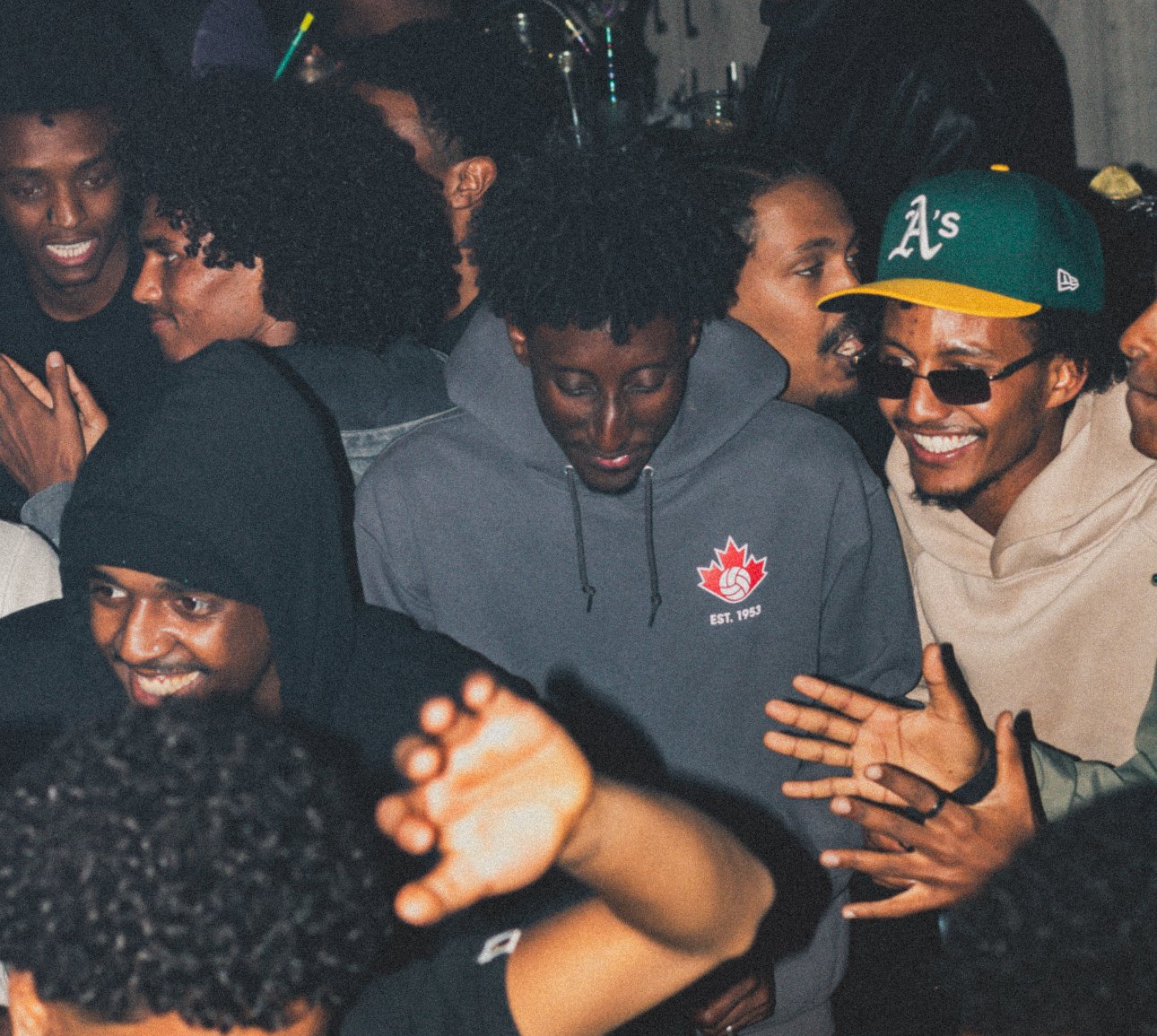 A group of young people socializing closely together at a crowded indoor gathering.