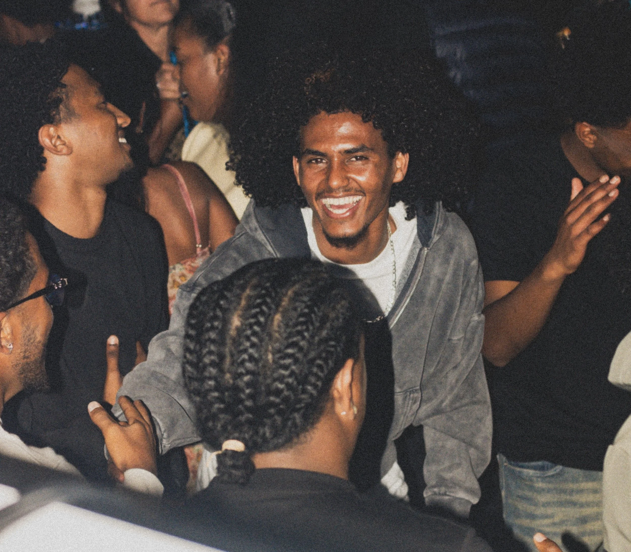 Group of people socializing at a party, with a smiling man with curly hair in the center.