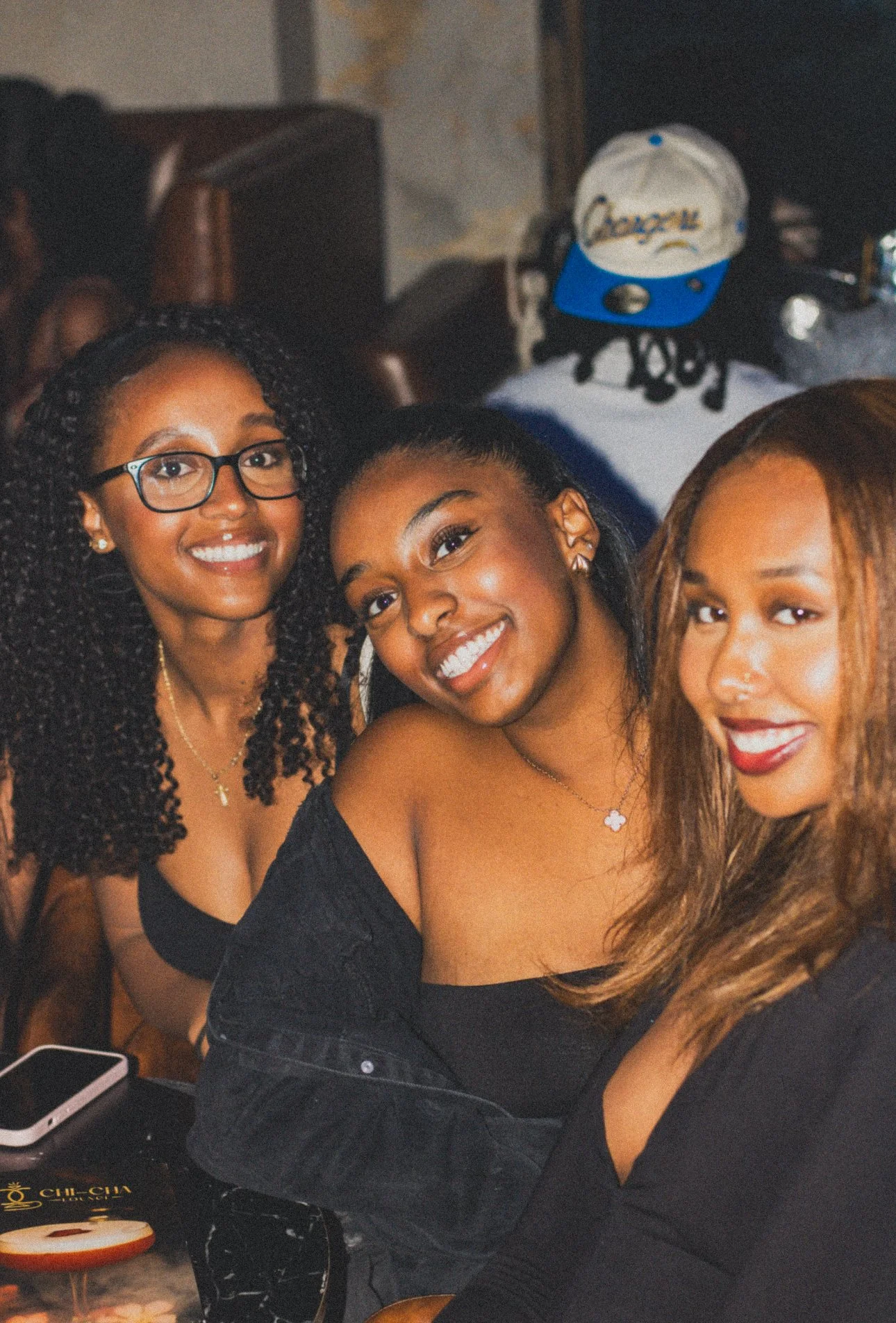Three young women smiling and sitting together in a restaurant or cafe.
