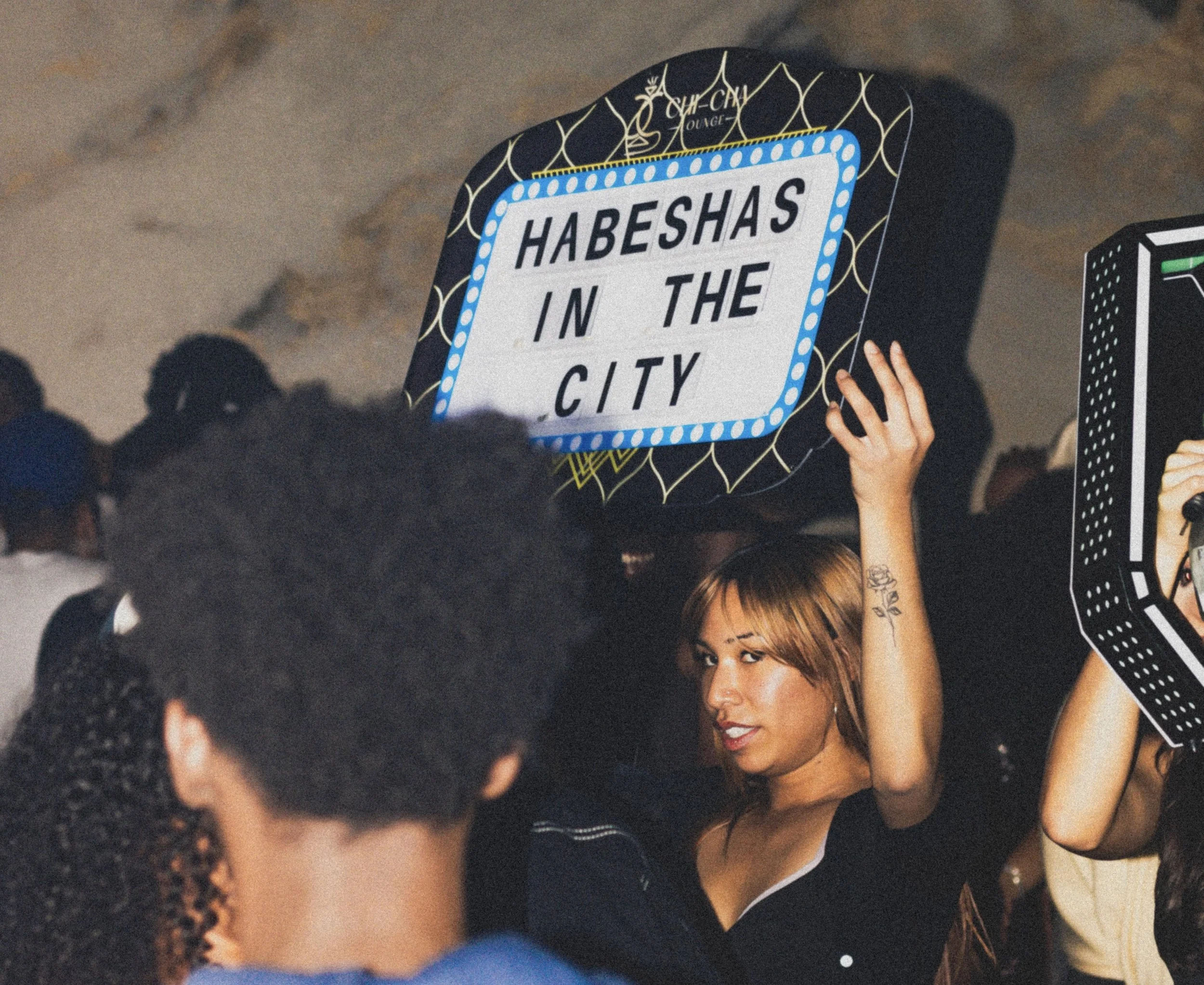 A woman holding a sign that says 'Habeshas in the city' during a crowd gathering or protest.