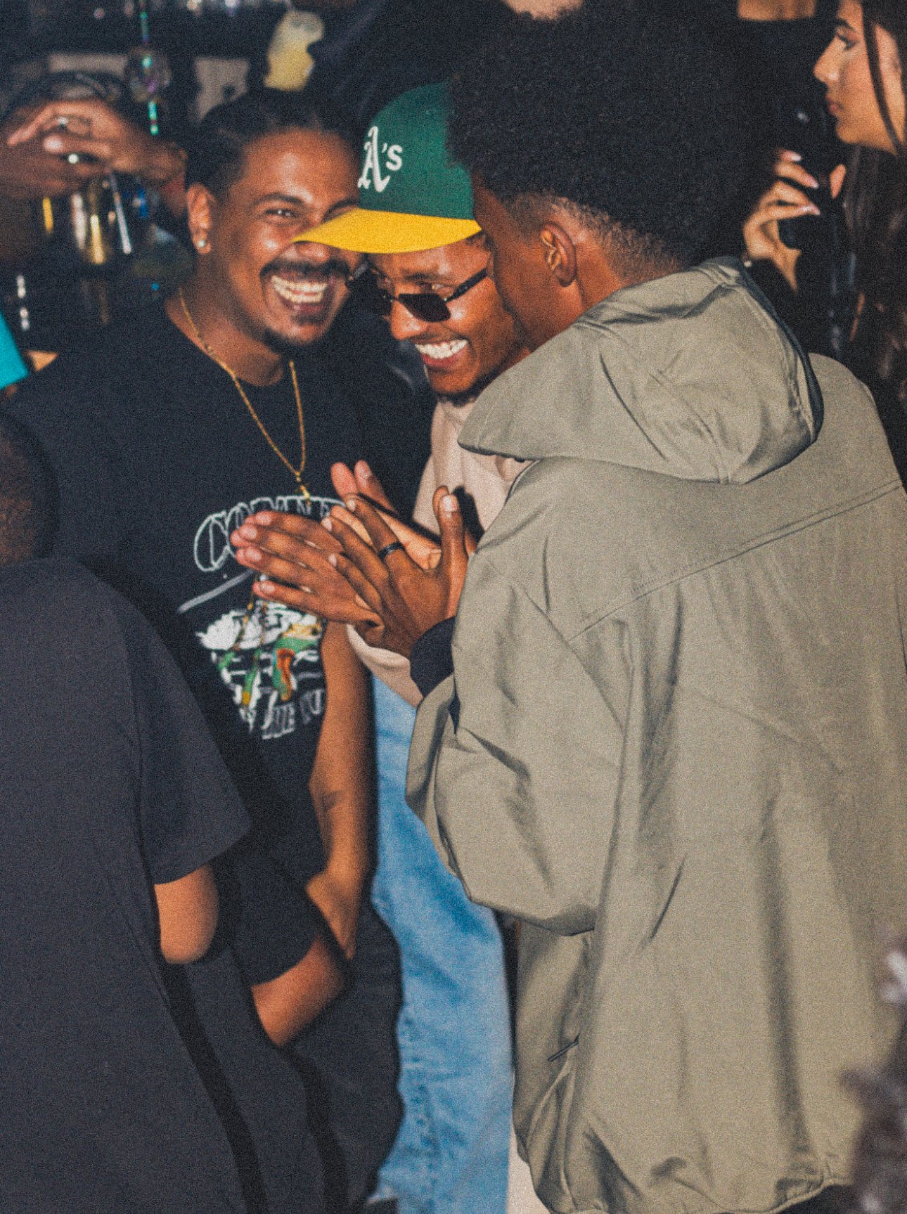 Group of three friends smiling and laughing together at a social gathering, engaged in a friendly conversation.