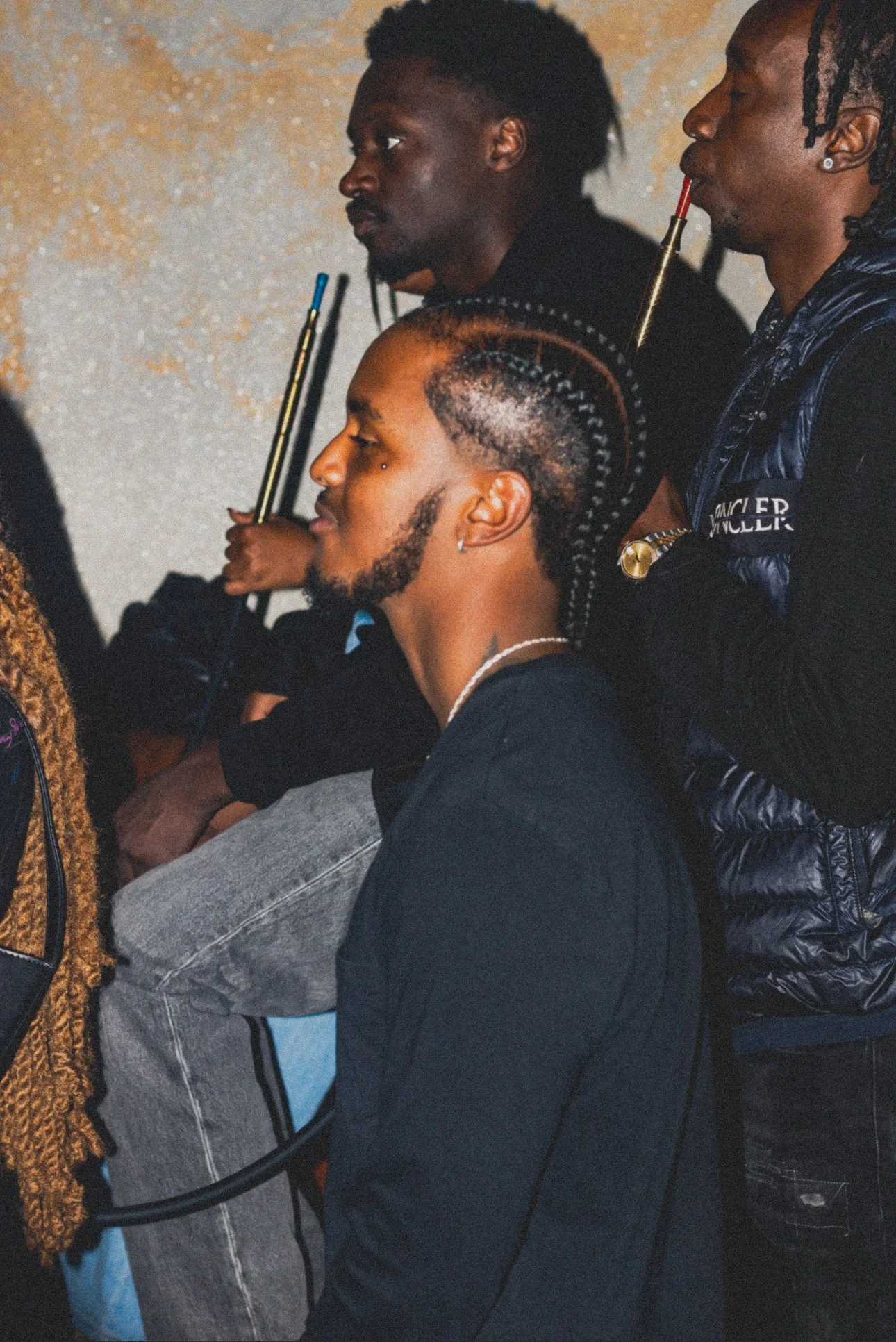 A group of three people sitting together, with two of them holding pool cues, against a textured wall.