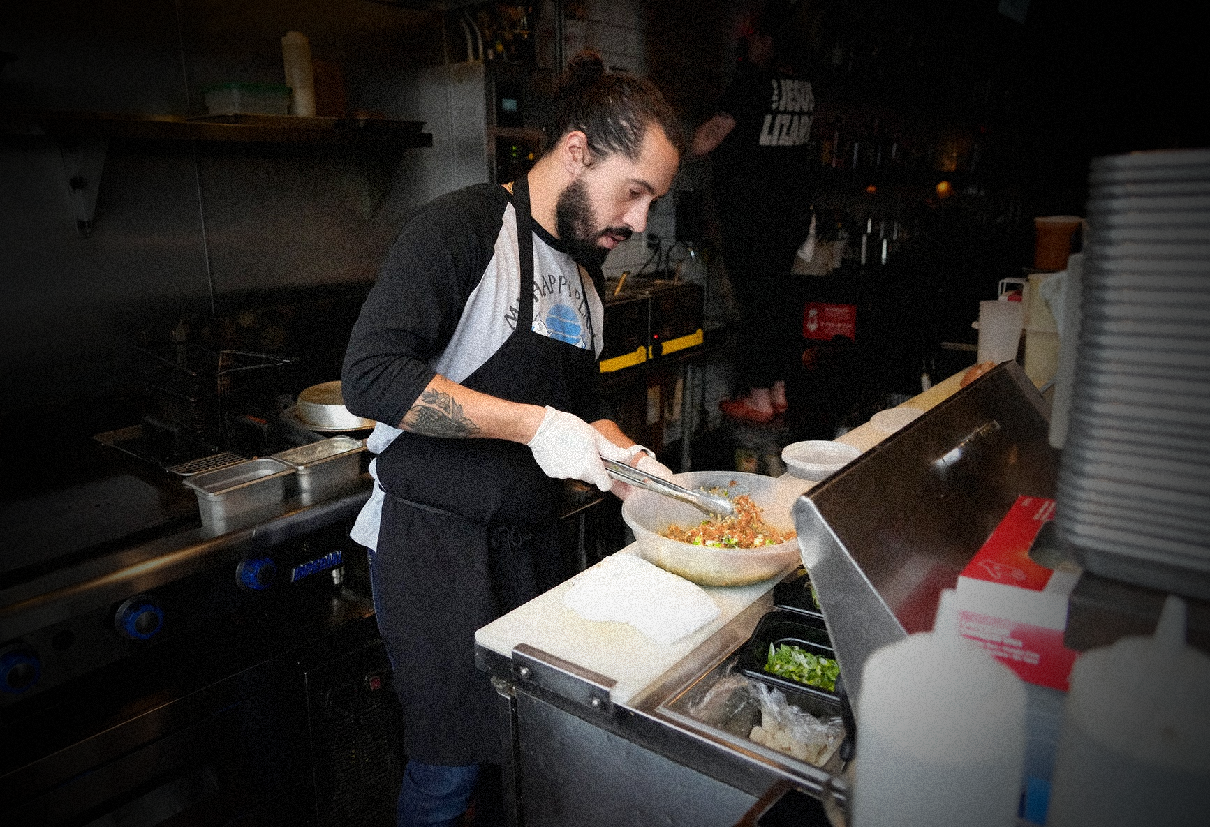 A man cooking in a professional kitchen preparing a dish in a large bowl.