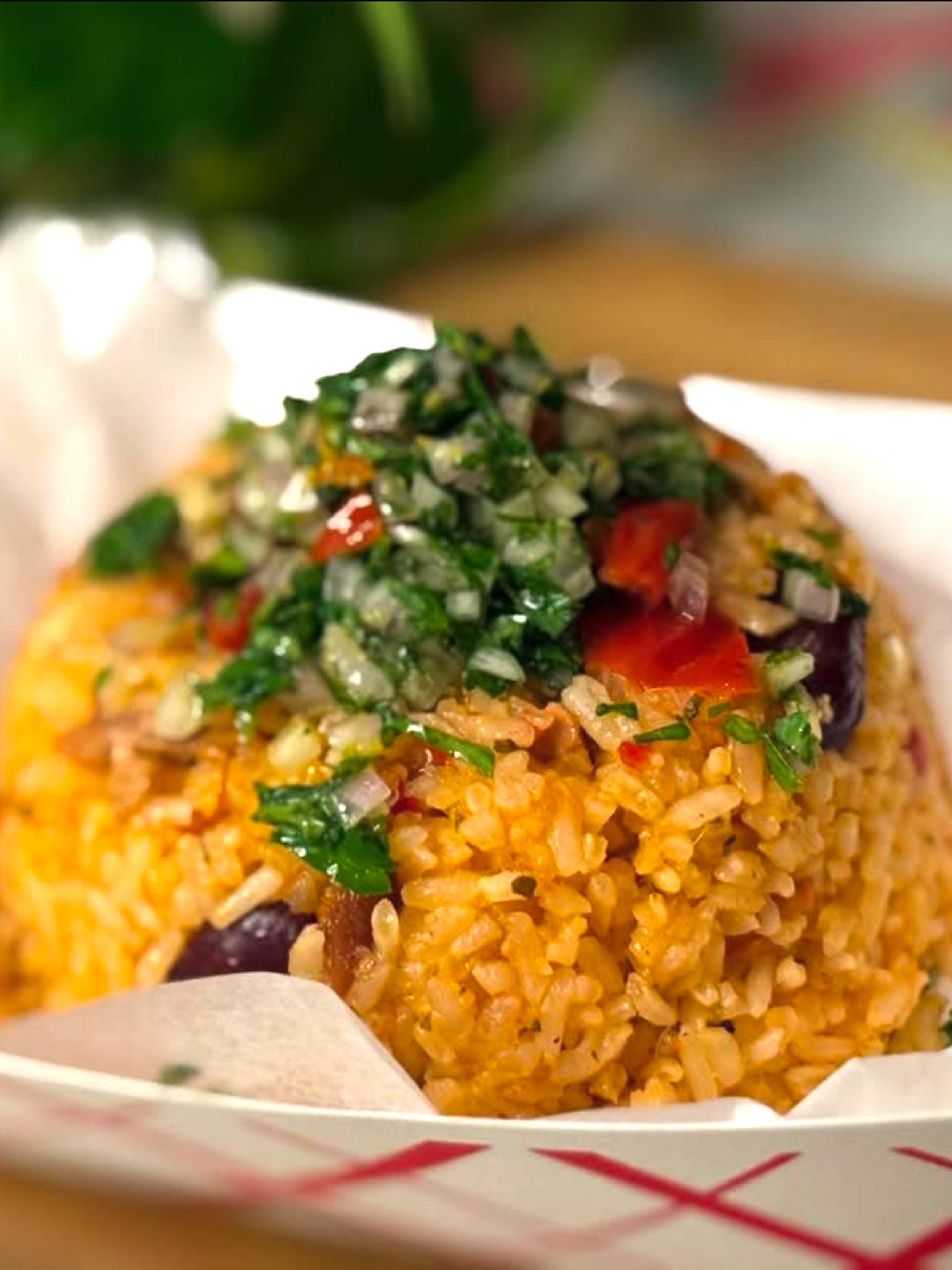 Close-up of seasoned rice topped with chopped fresh herbs and diced vegetables in a white container.