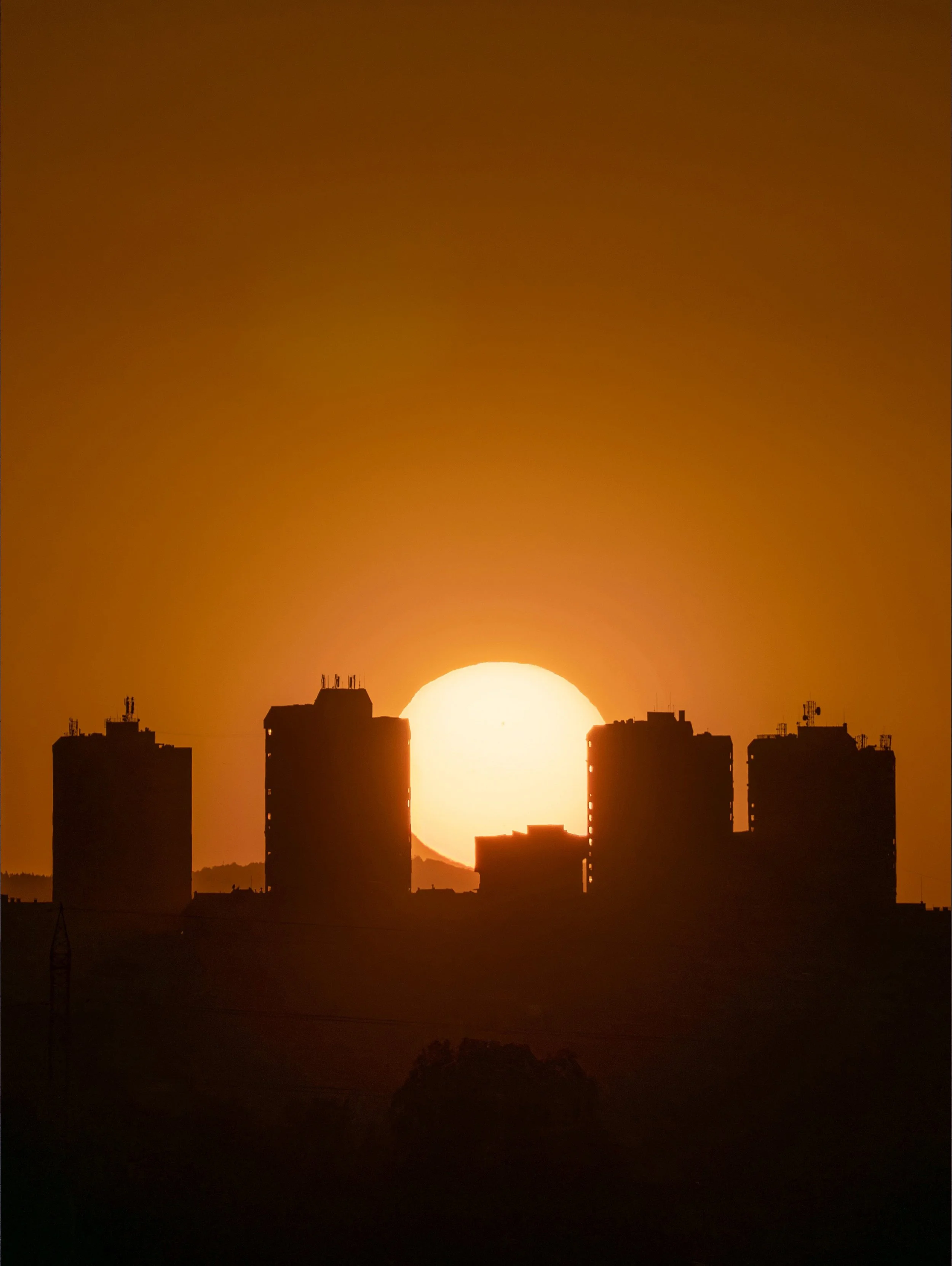 Sun setting behind silhouetted city buildings at dusk.