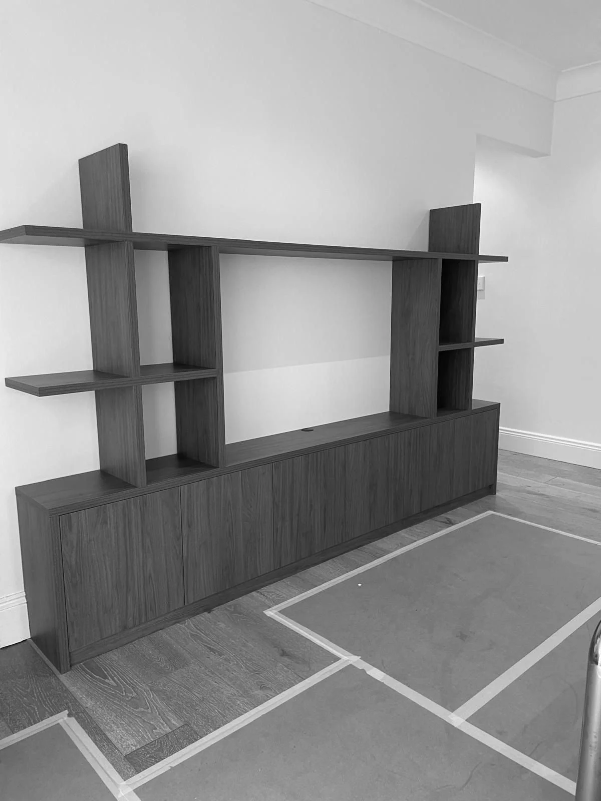 A modern walnut wooden tv wall unit with open shelves and cabinet doors, placed against a white wall in a room with wooden flooring.