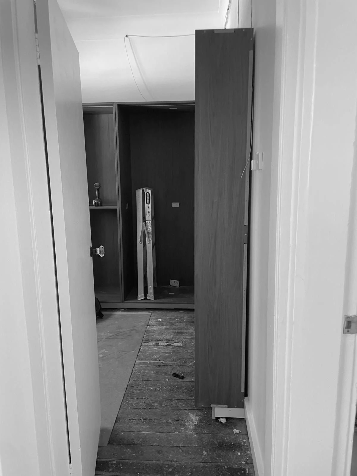A doorway leading to a room under renovation with wooden flooring, a partially built wardrobe, tools, and construction materials visible inside.