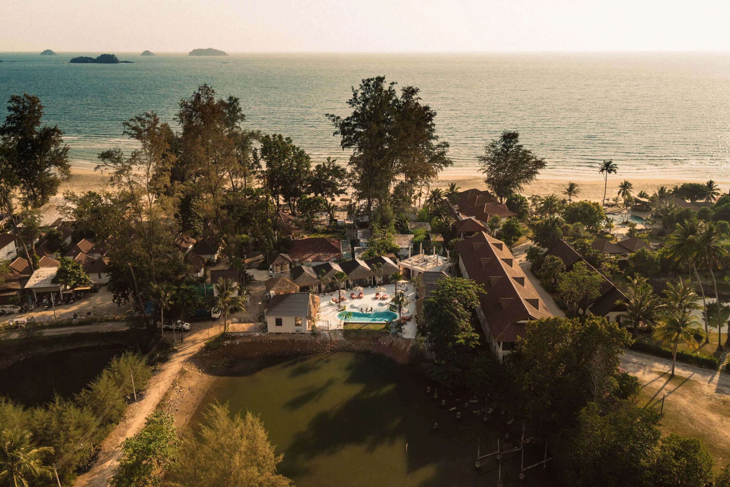 Aerial view of a coastal resort with a swimming pool, surrounded by trees, small buildings, and the ocean in the background. Koh Chang, SAGA, oasis, Klong Prao Beach, Sol Beach