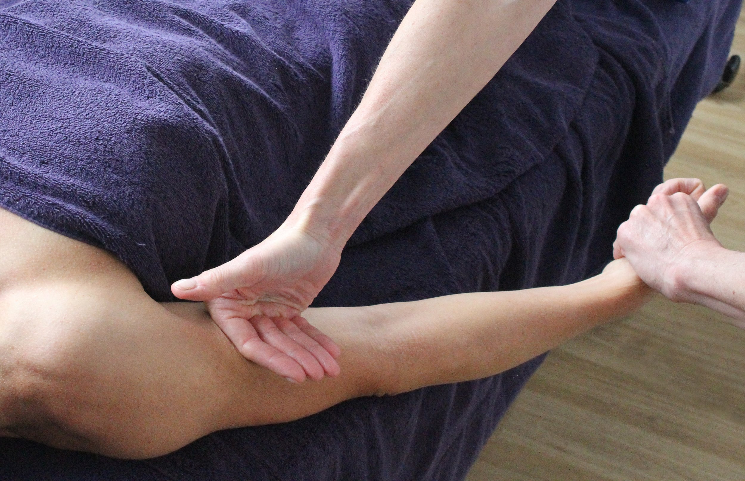 Person receiving physical therapy or massage while lying on a bed or table, with hands of therapist applying pressure to their thigh.