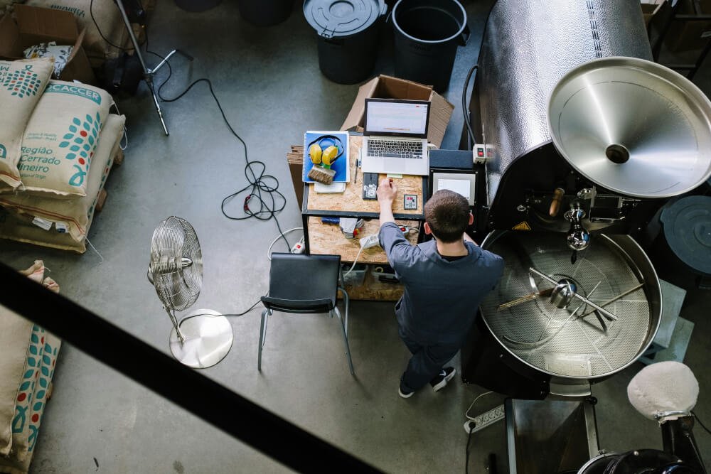 Ein Mann arbeitet in einer Kaffeerösterei, die wie ein Labor aussieht und aus der Vogelperspektive gesehen ist.