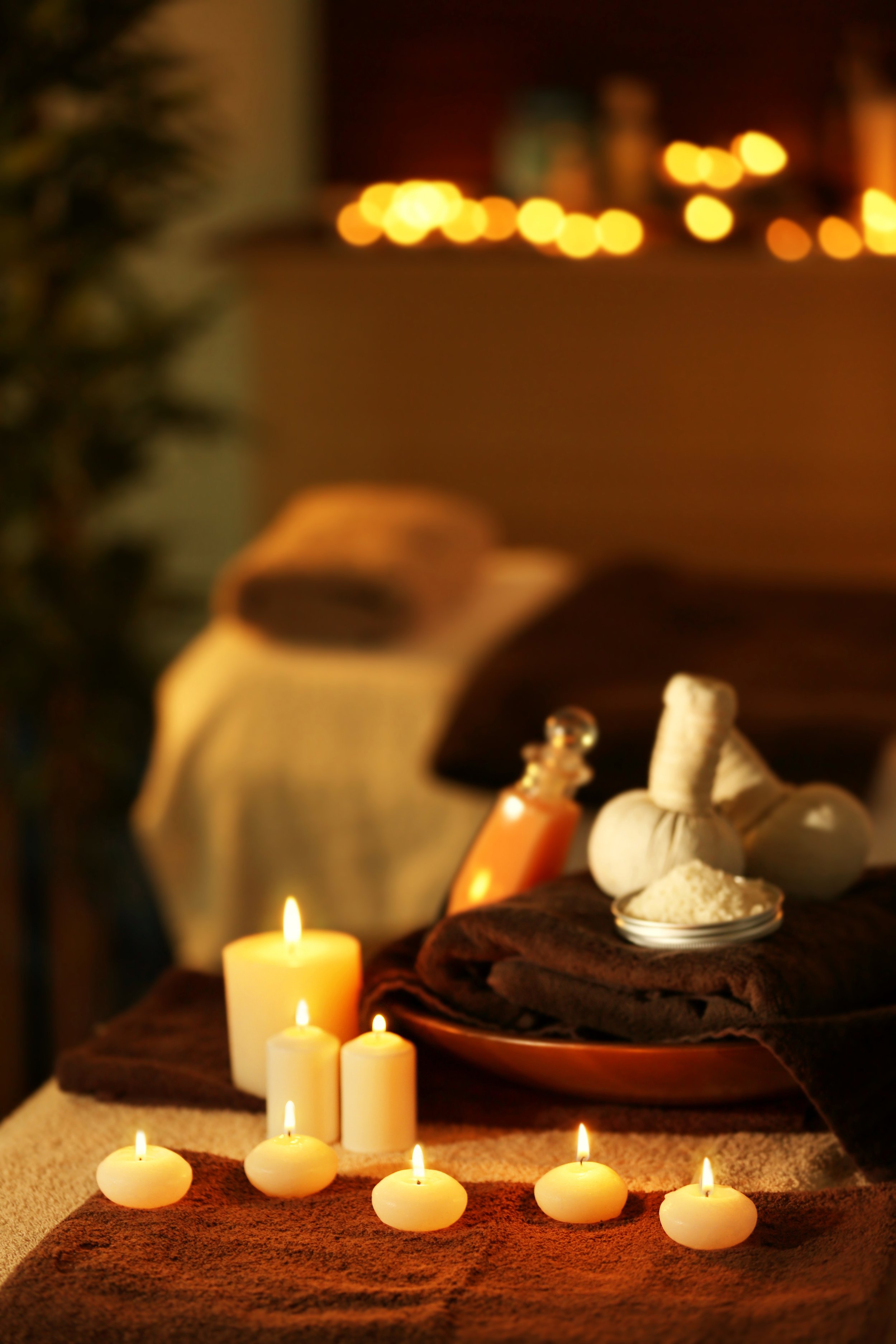 A spa or massage setup with lit candles, herbal compresses, and a bowl of herbs, creating a relaxing atmosphere.