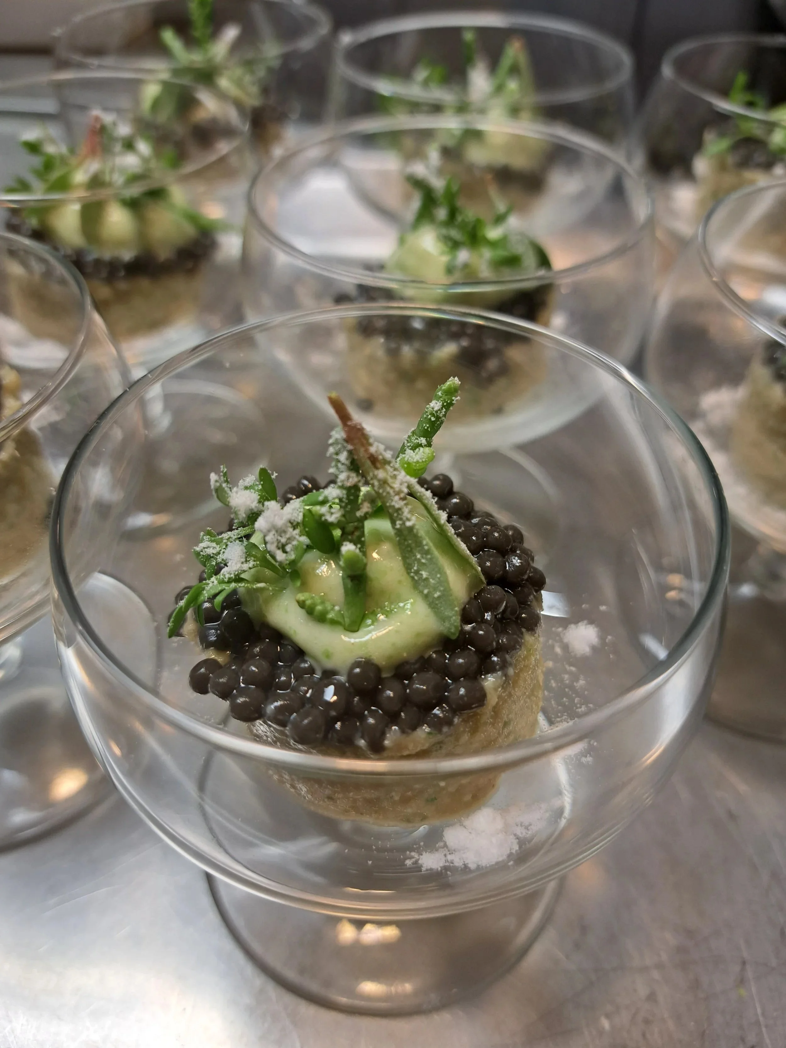 Elegante mini-desserts met groene decoratie, zwarte parels en poedersuiker in heldere glasjes.