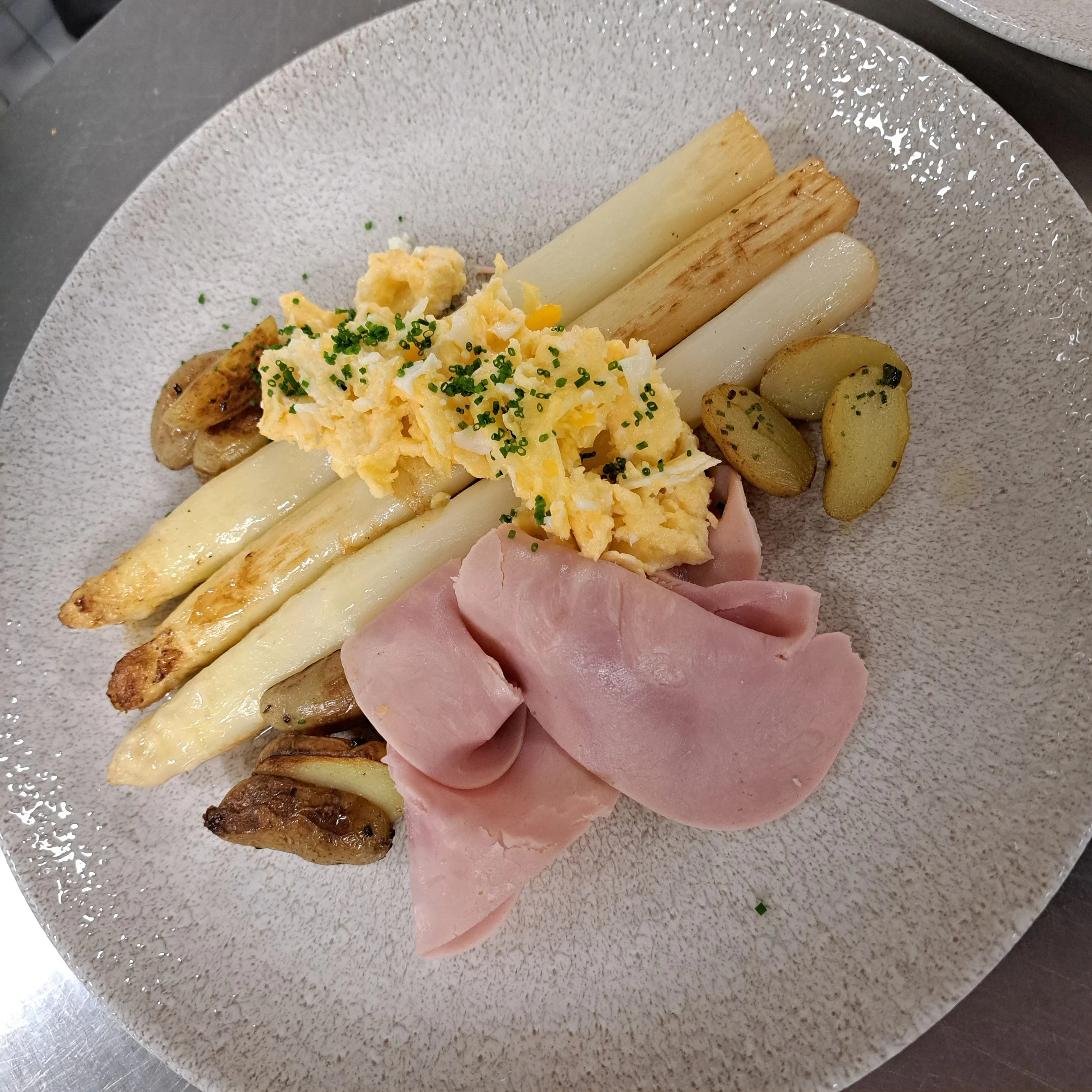 Een bord met gegrilde asperges, gekookte aardappelen, ham en een omelet met bieslook
