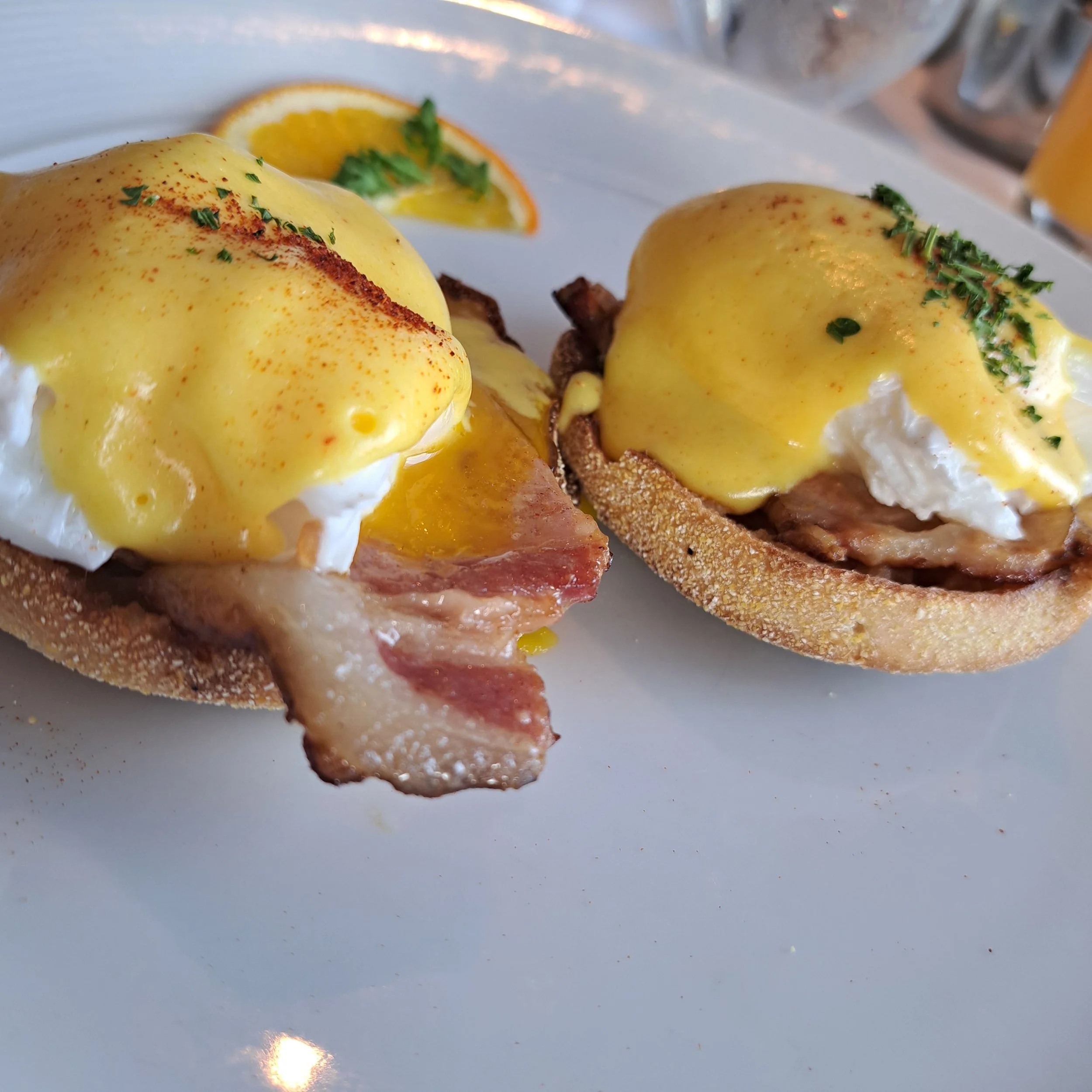 Eggs Benedict met hollandaise saus en verse kruiden, geserveerd met een stukje gerookte zalm en een schijfje sinaasappel.