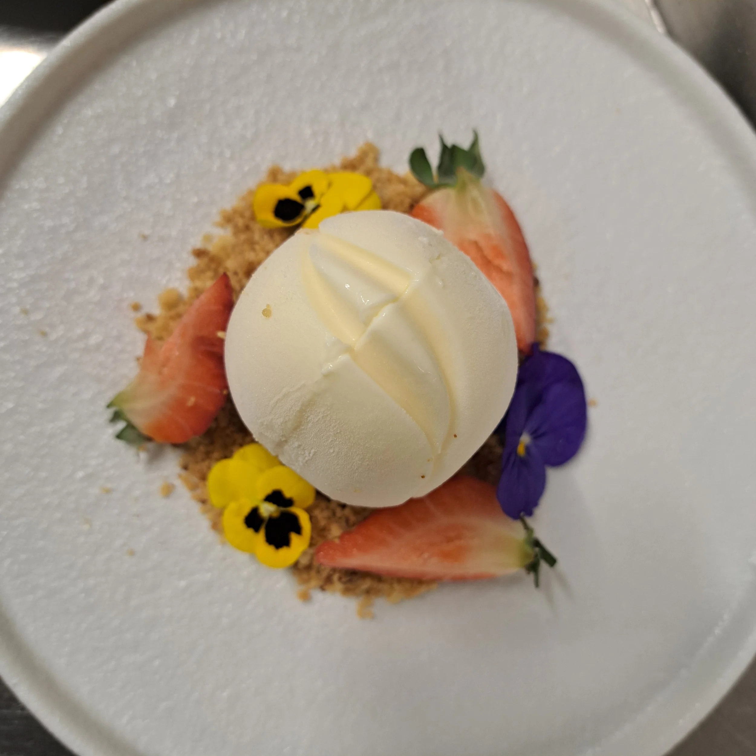 Close-up van een dessert met een witte chocolade decoratie, aardbeien, blauwe bloemen en kleurrijke decoraties op een witte kom.