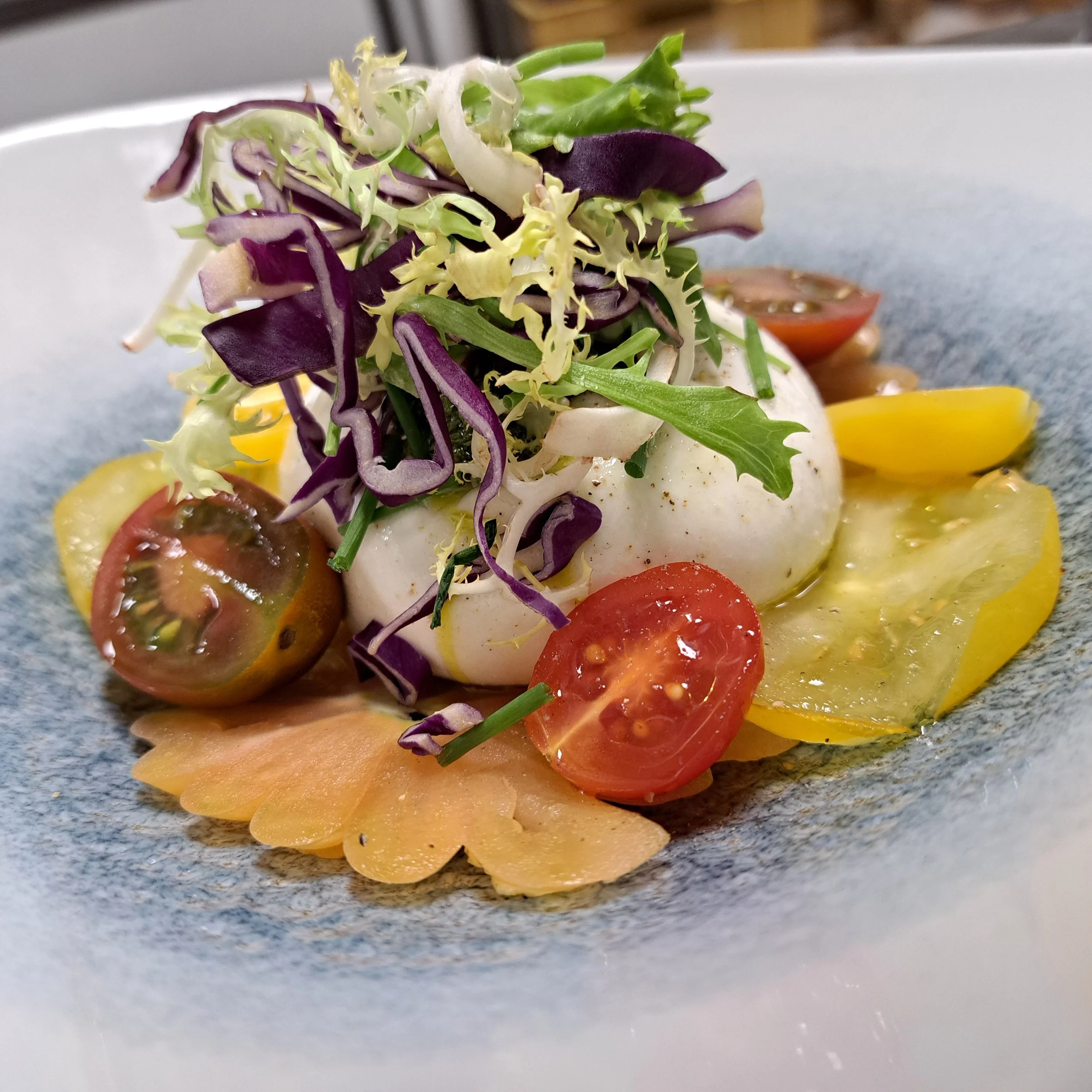 Salade met diverse groene bladgroenten en tomaat op een bord.