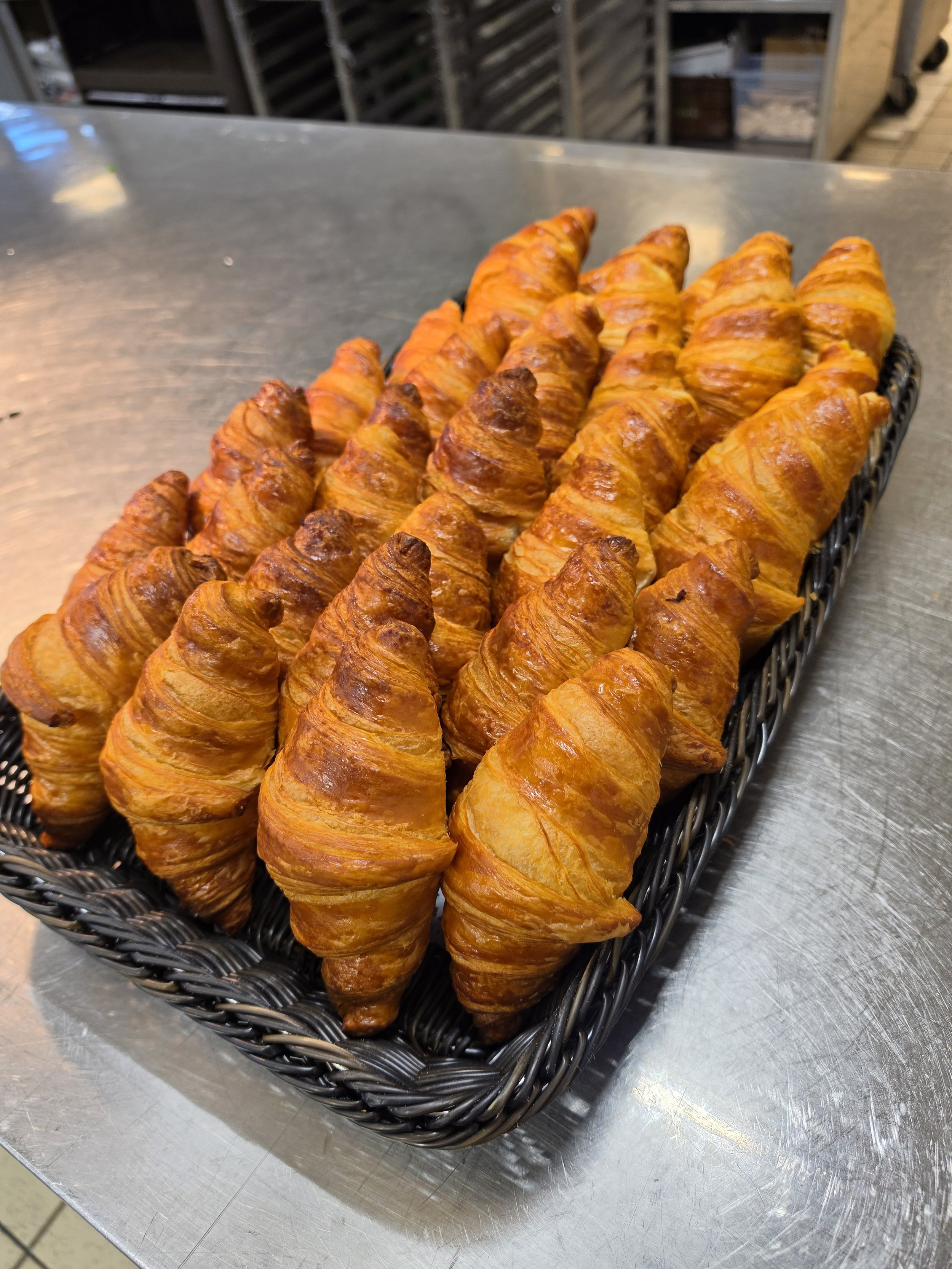 Een mand met versgebakken croissants op een metalen tafel.