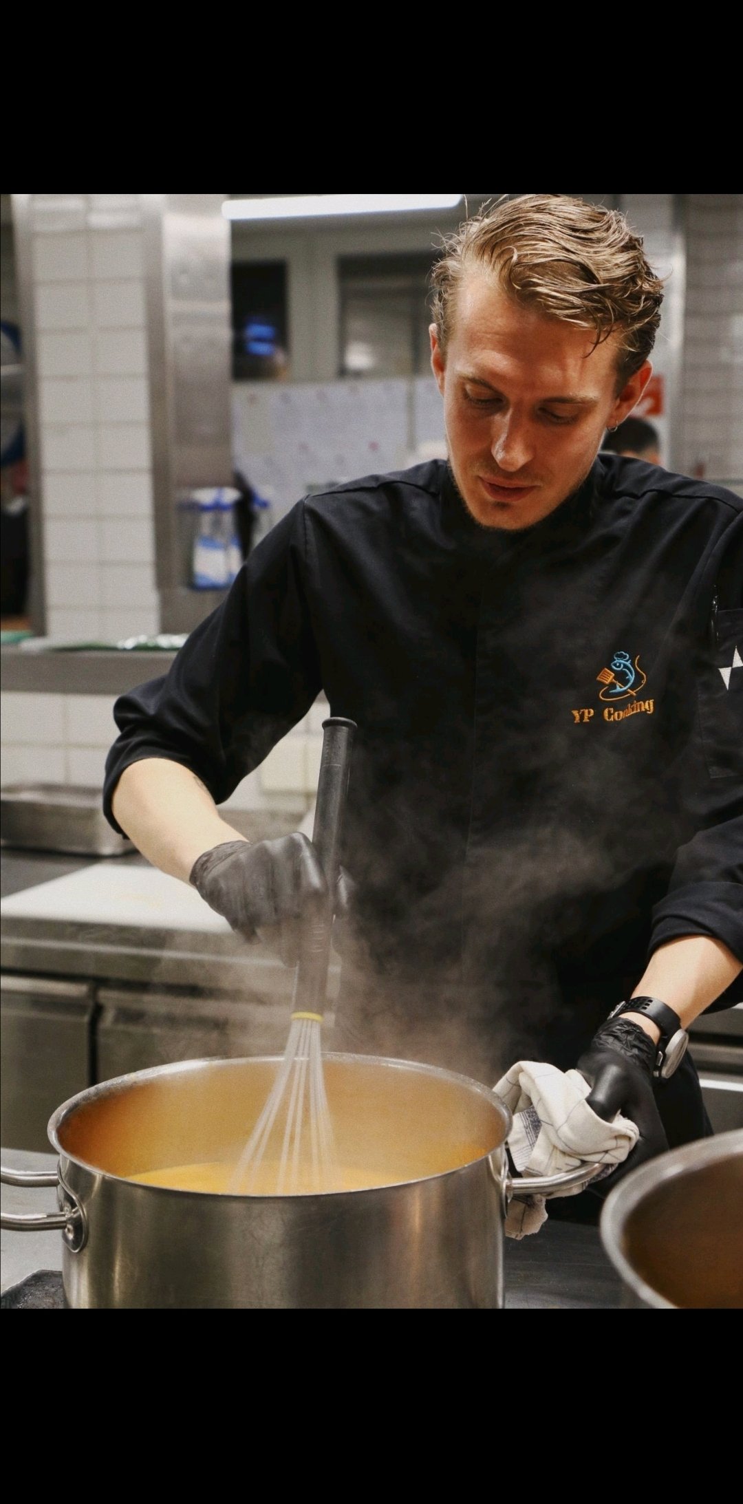 Yannick Presser kookt in een professionele keuken, roert een grote pan voor een catering voorbereiding, professioneel gekleed met eigen merk.