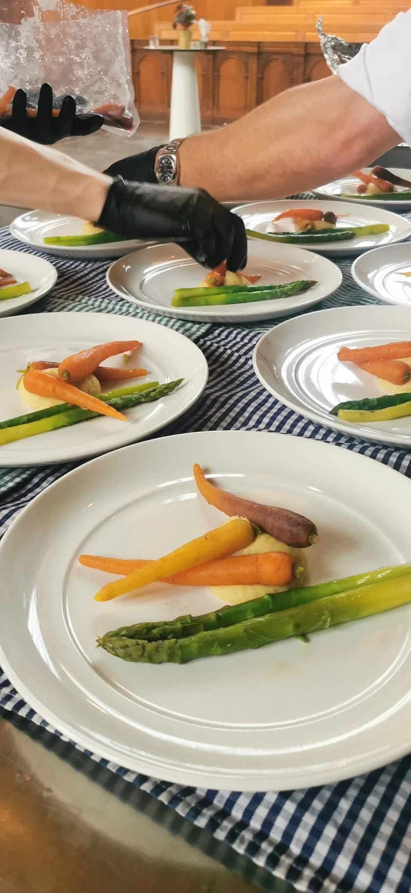 Chef bereidt groentegerechten met wortelen en asperges op witte borden tijdens een chef-kok event.