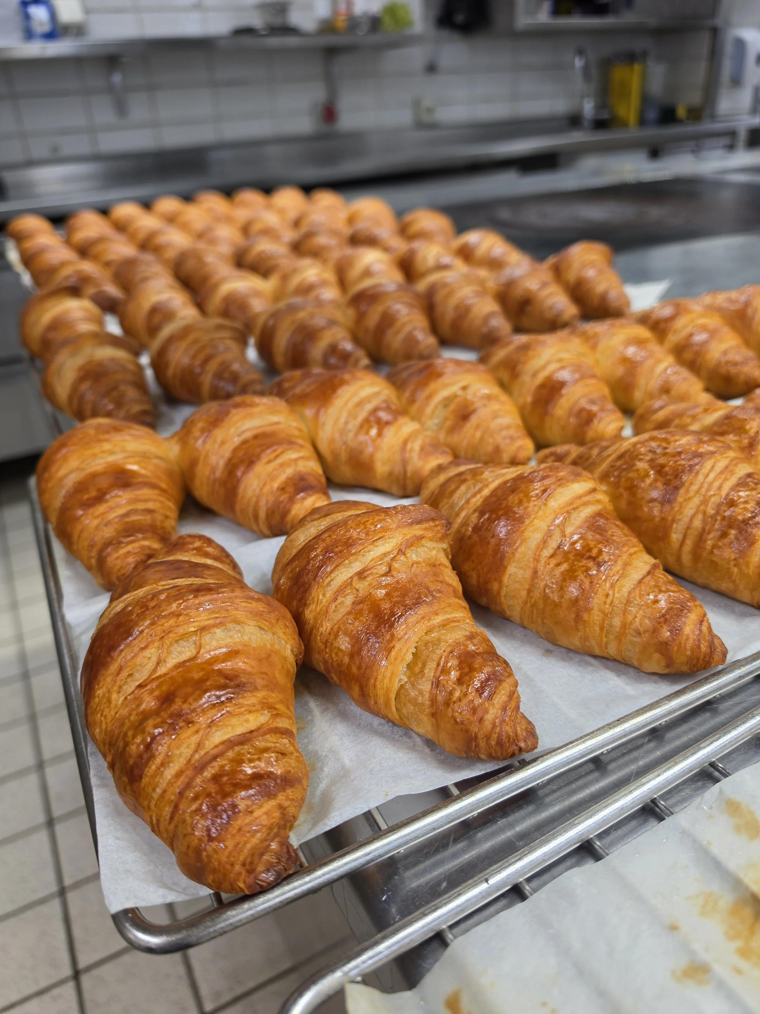 Verscheidene goudbruine croissants liggen op een bakplaat met bakpapier in een bakkerij of keuken.