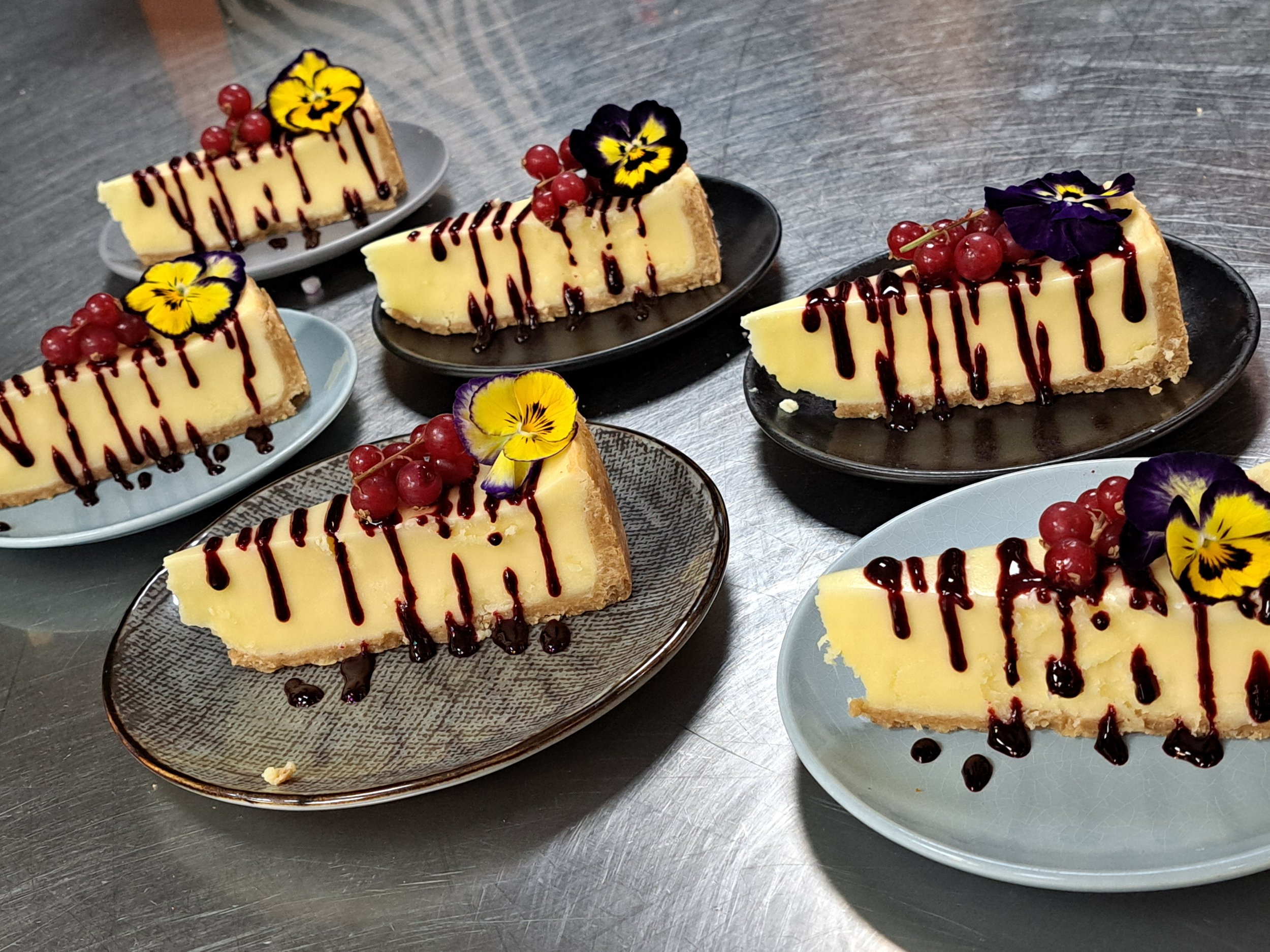 Bewezen plakjes mini cheesecakes met zwarte bessen, rode bessen, chocolade druppels en viooltjes op verschillende kleine borden.