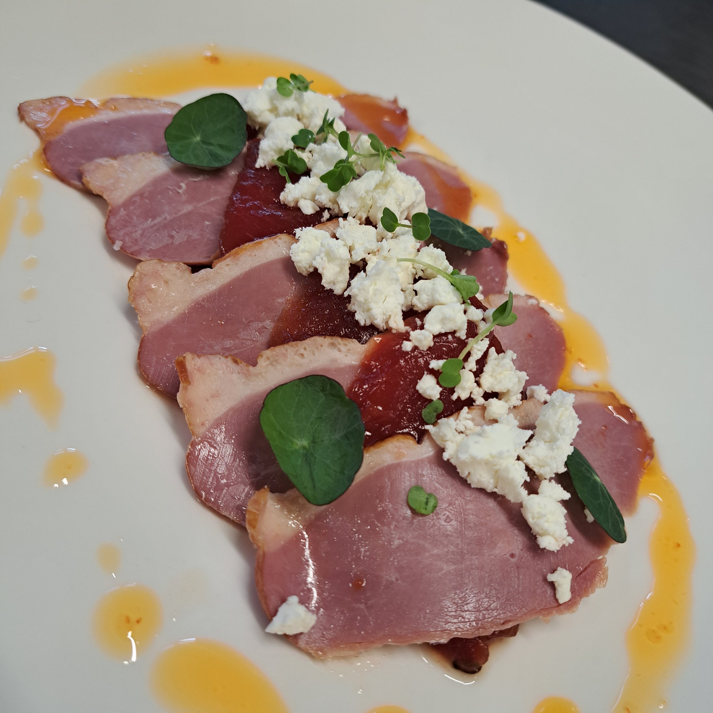 Versneden ham met crumbles, microgroenten en een saus op een wit bord