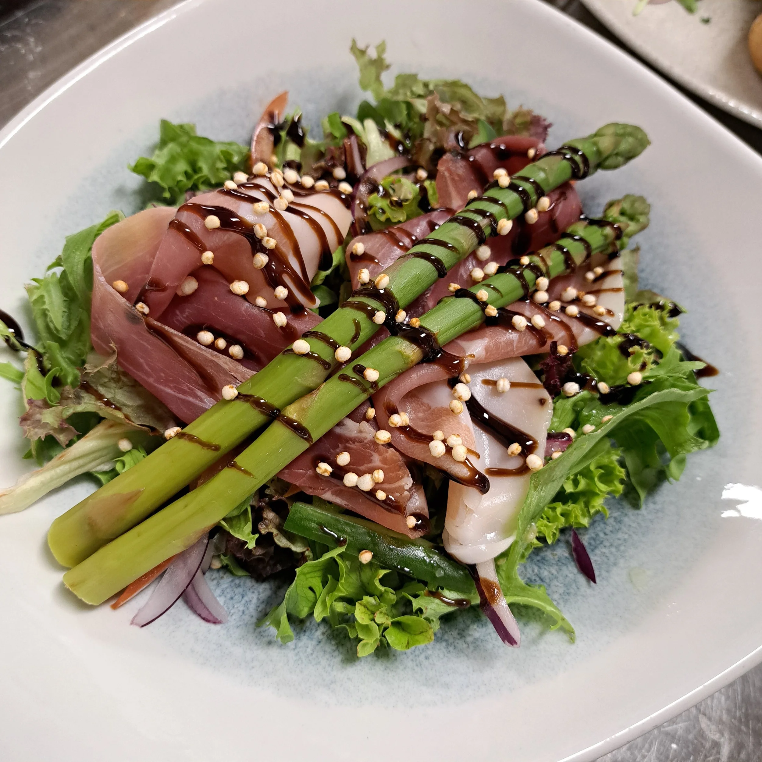 Salade met groene asperges, gemengde bladgroenten, ham, balsamico dressing en korrels.