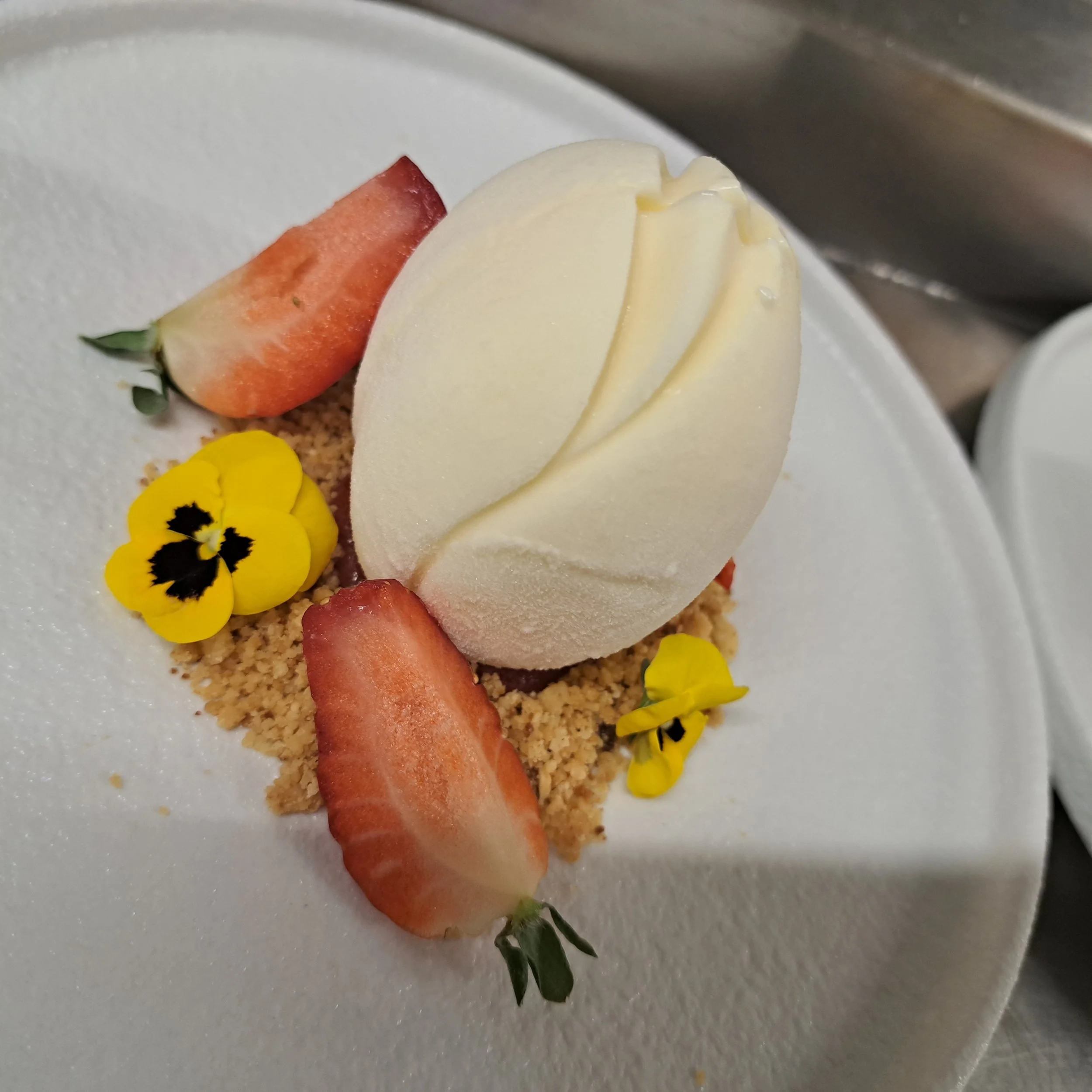 Een stuk aardbei, een scheermesje met witte crème en gele bloemen op een wit bord.