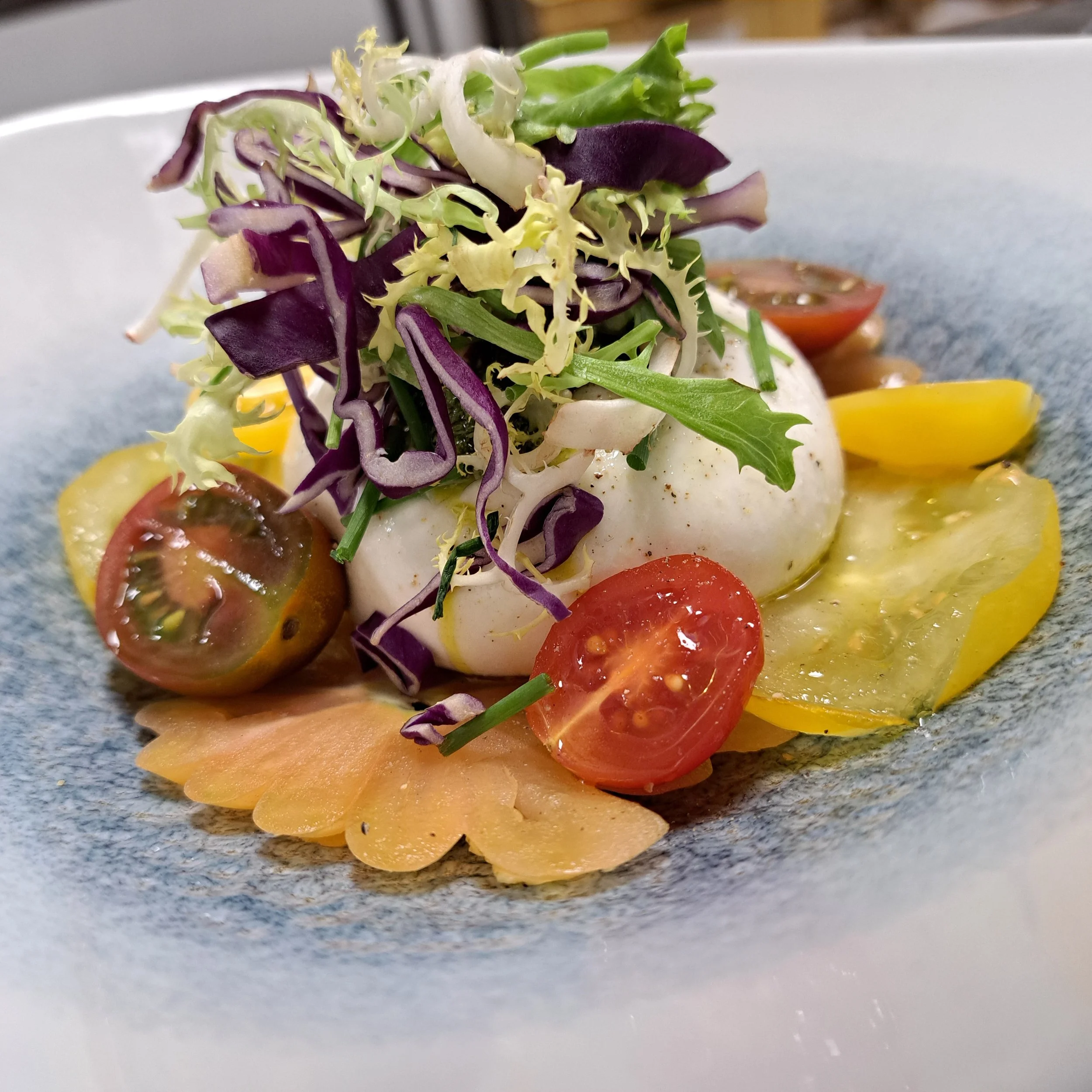 Een bord met een salade bestaande uit diverse kleurrijke groenten, zoals tomaat, komkommer, paprika en verschillende bladgroenten.