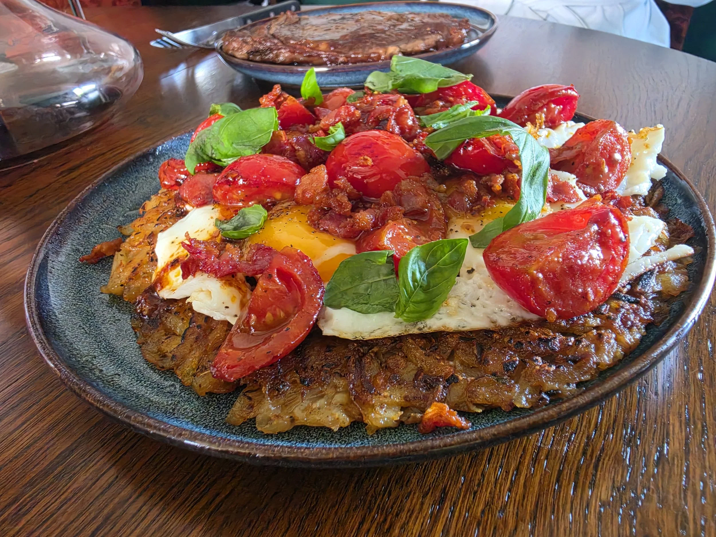 Gerecht met gepocheerd ei, tomatensaus, basilicum en knapperige aardappelrasp op een zwarte bord op een houten tafel.