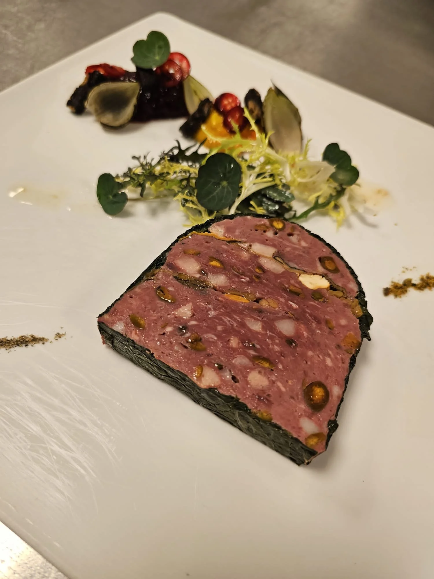 Gesneden stuk foie gras met pistachenoten en een salade met microgroenten en bessen.