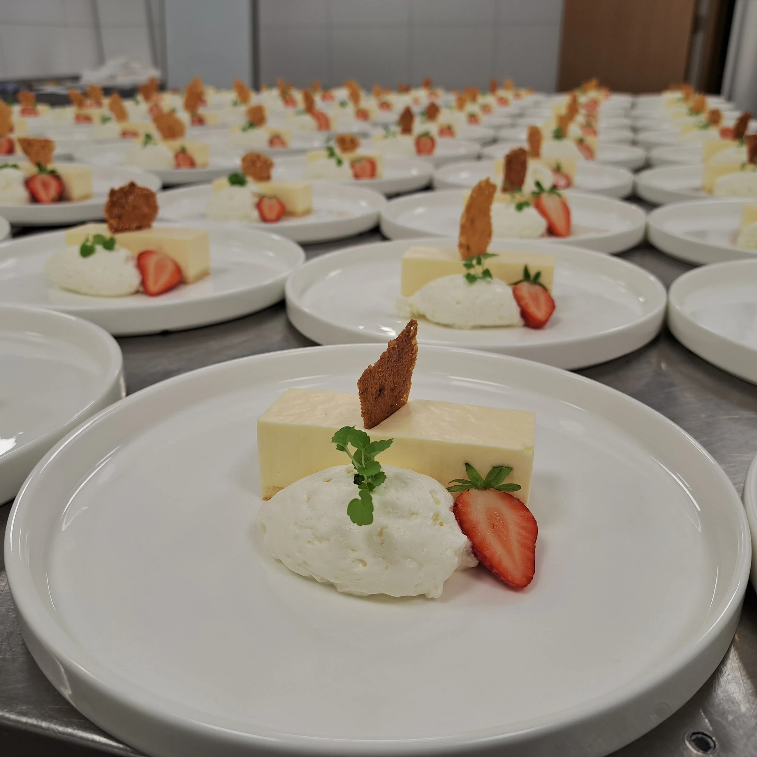 Desserts op witte borden, inclusief witte chocolade, aardbeien en stukjes krokante koek.