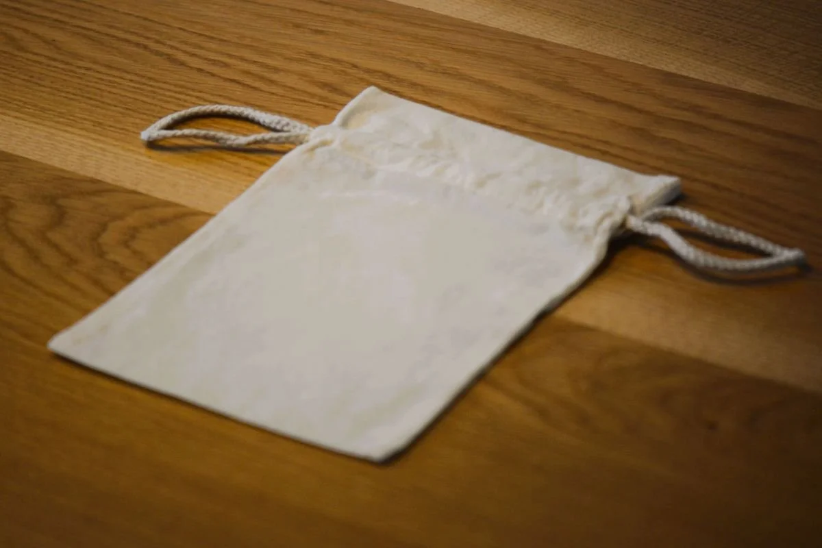 Baumwollbeutel mit Kordelzug in Rückansicht - ohne Aufdruck - auf Holztisch.