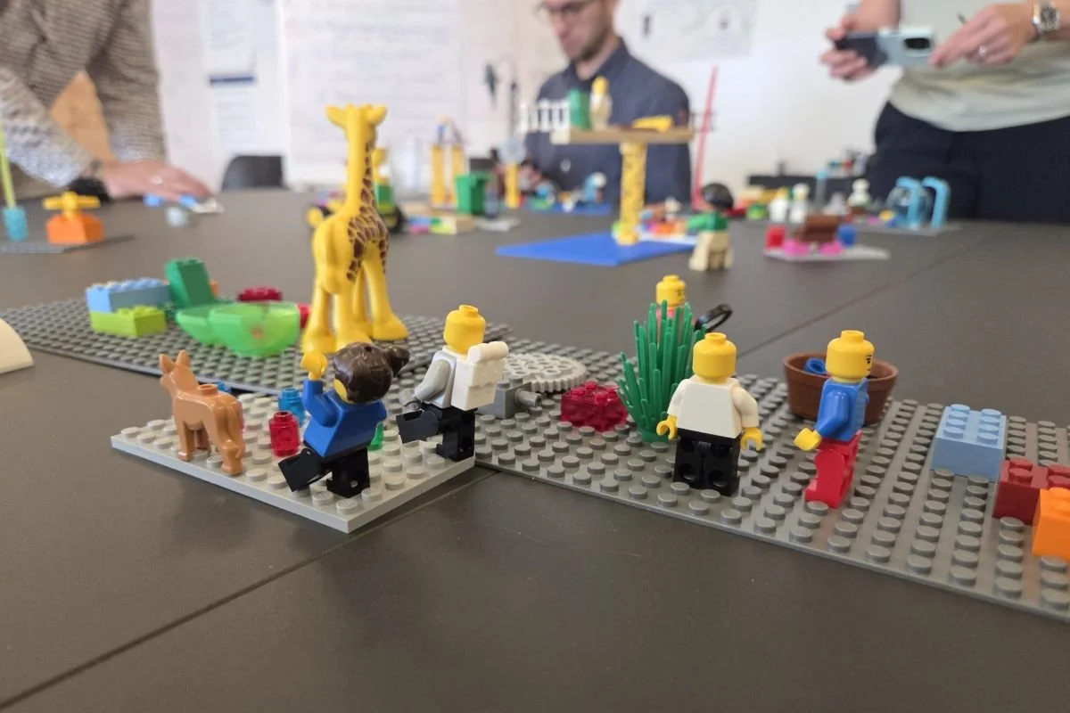 LEGO® SERIOUS PLAY® Workshop mit verschiedenen LEGO‑Modellen und Figuren auf einem Tisch.