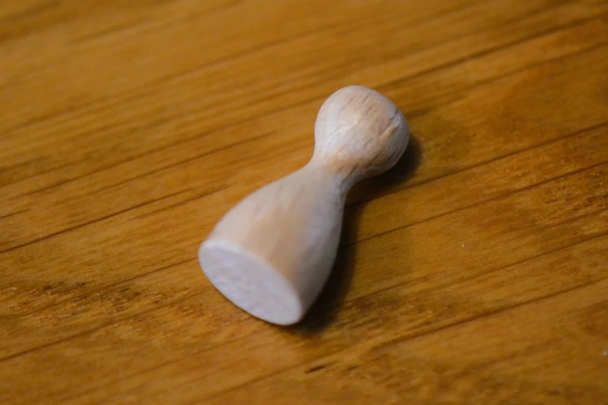 Halma‑Spielfigur aus naturbelassenem Holz liegend in Draufsicht auf Holztisch.