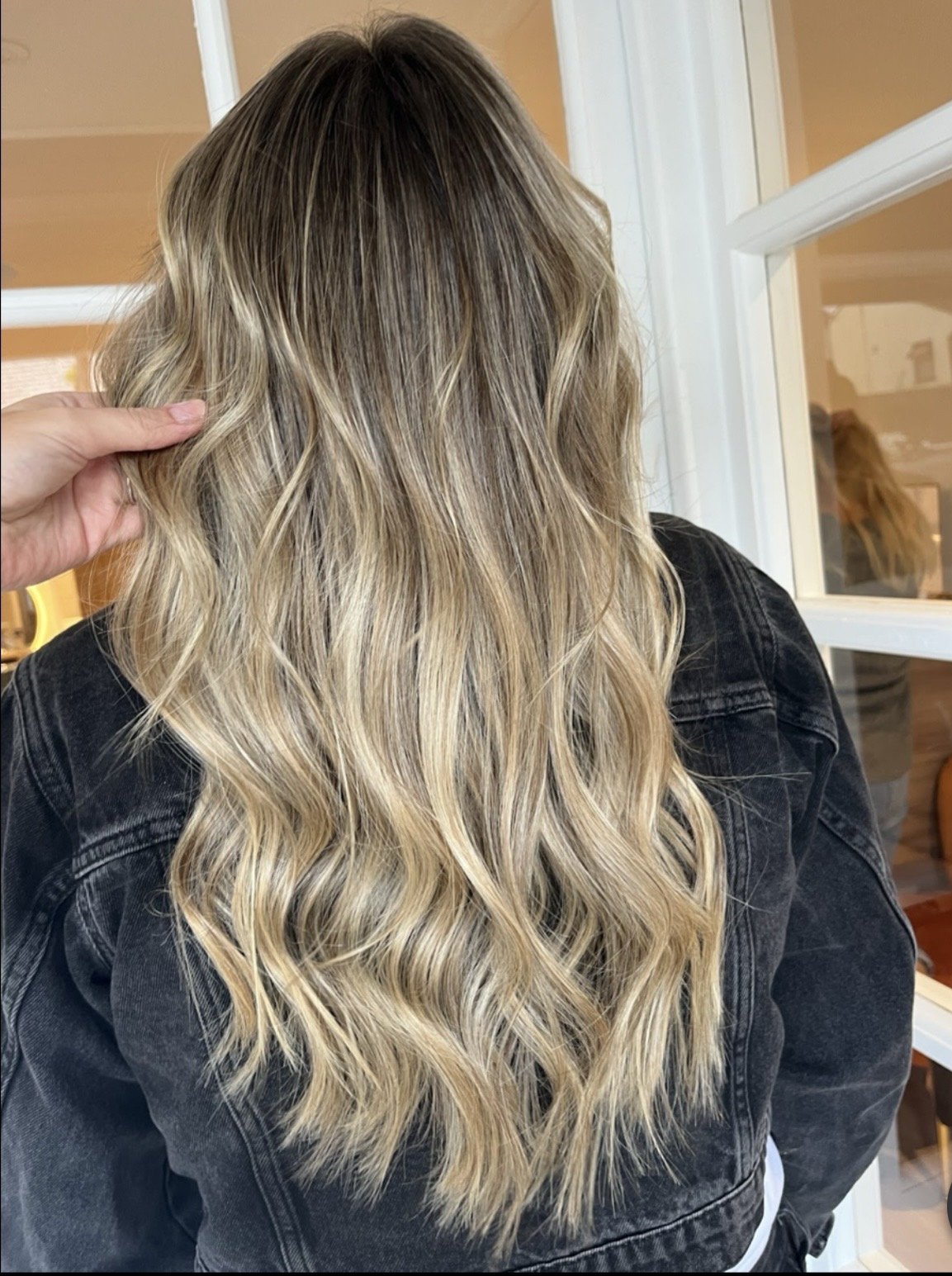 Back view of a woman with long, wavy blonde hair wearing a black denim jacket.