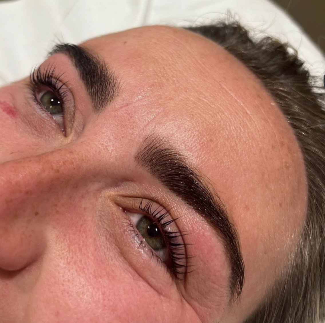 Close-up of a person's face showing well-groomed eyebrows and green eyes, with a focus on the eyebrows and skin texture.