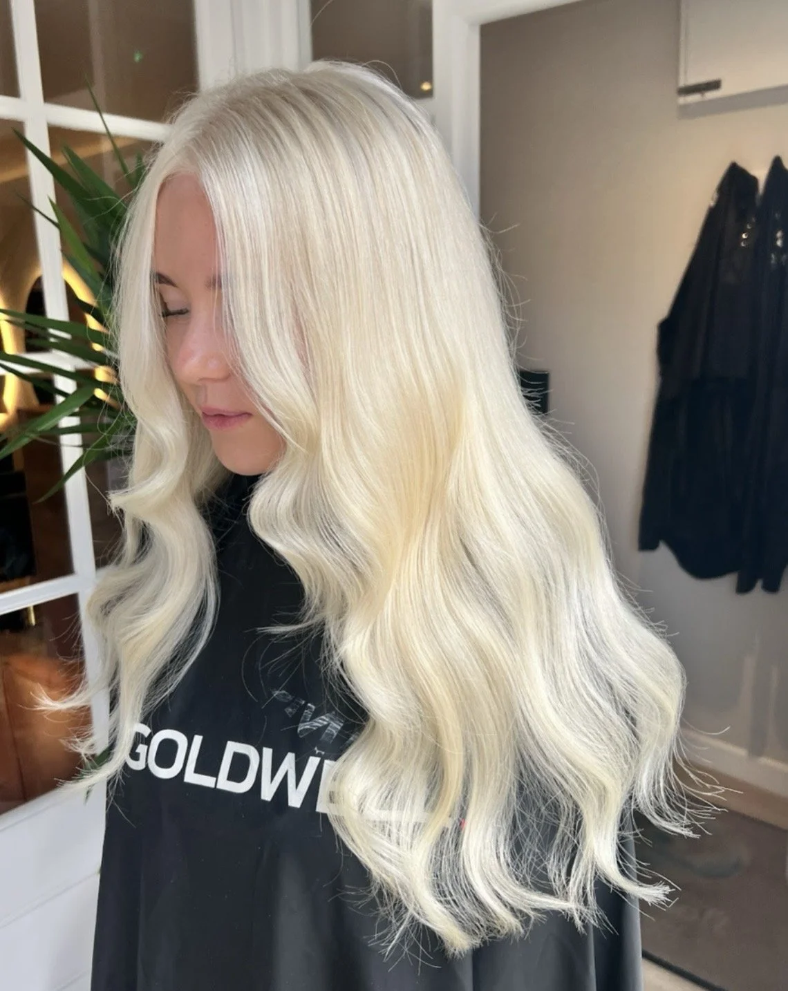 Woman with long, wavy, platinum blonde hair standing indoors.