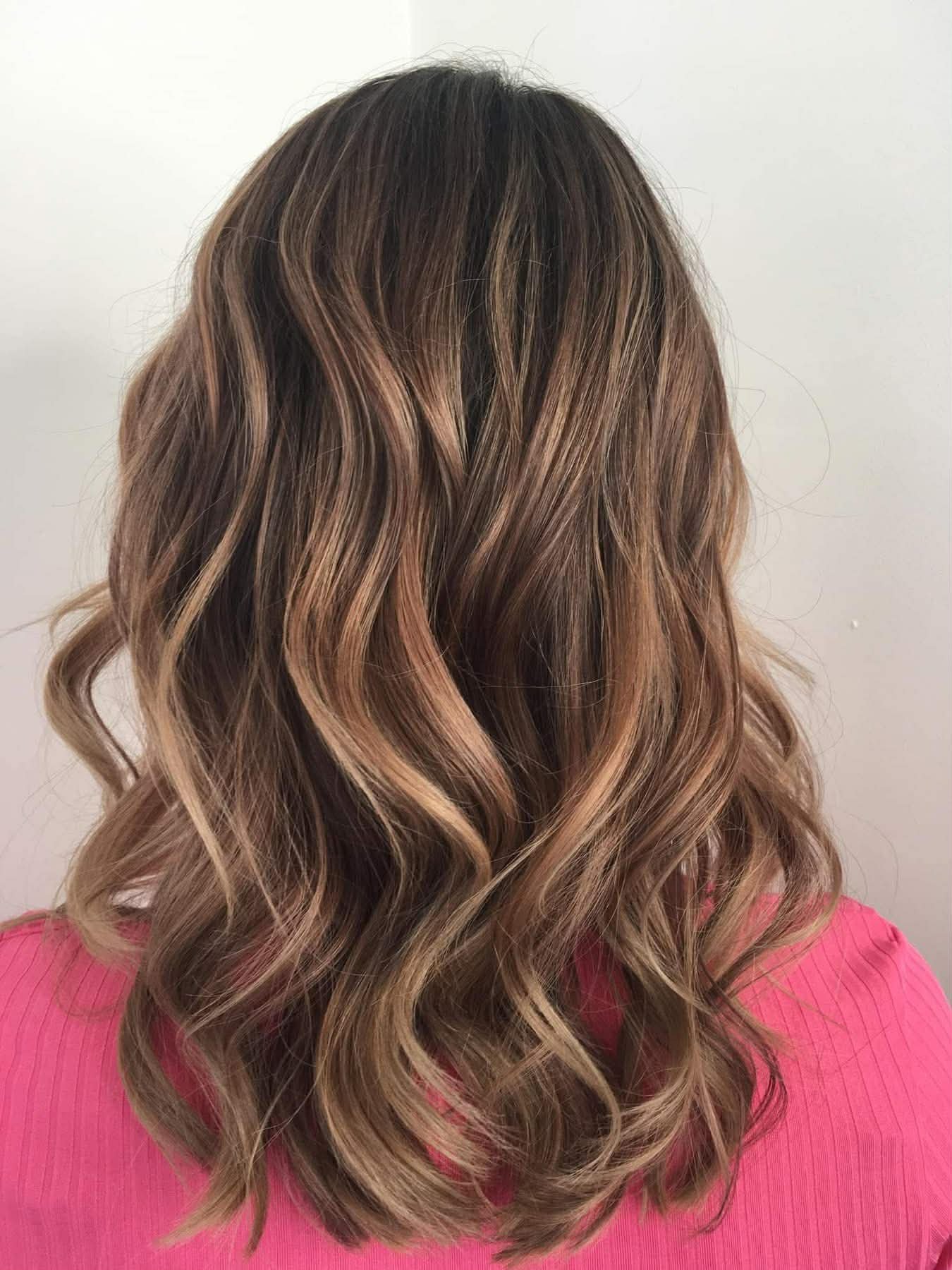 Wavy, light brown hair with blonde highlights, viewed from the back, on a person wearing a pink top.
