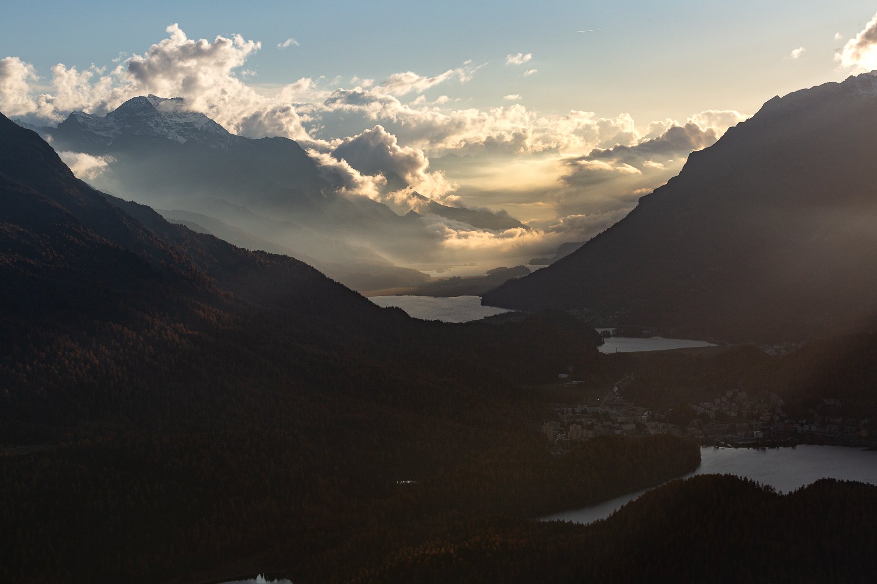 Mountain landscape during sunset with clouds, lakes, and forests in the valleys.