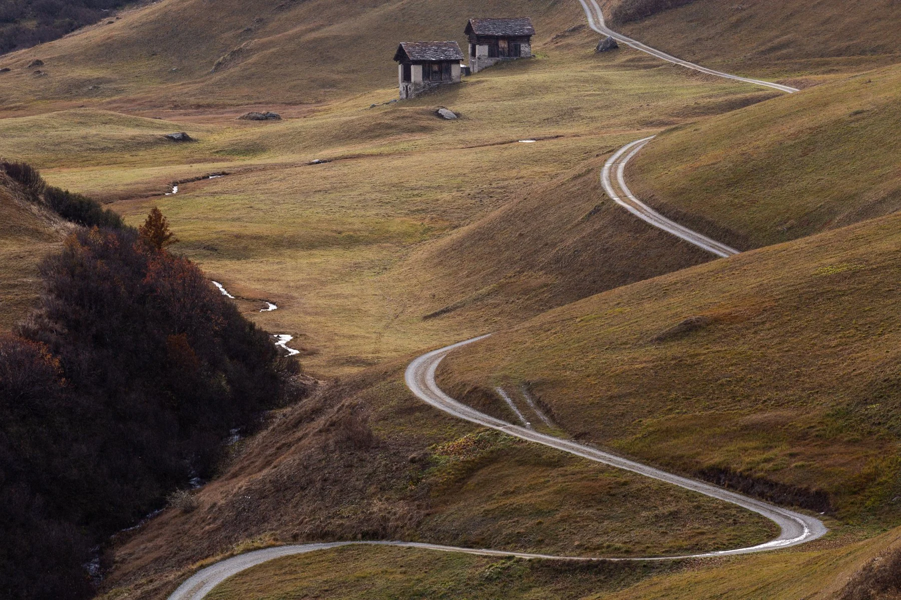 Winding dirt road through rolling hills with two small houses in the distance
