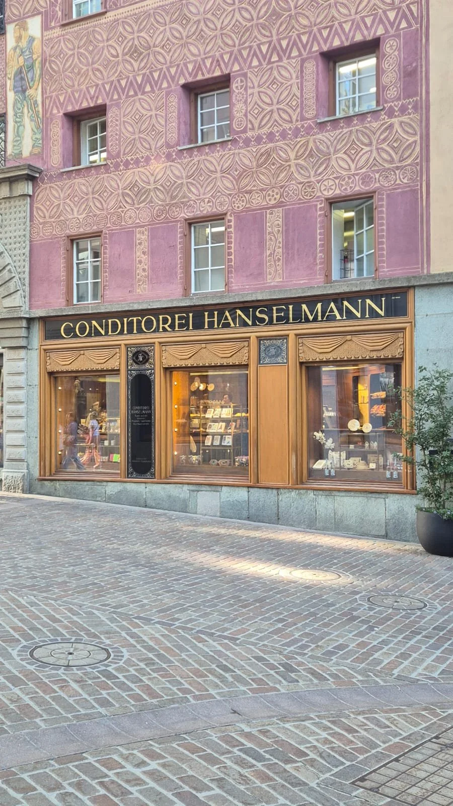 The storefront of Conditorei Hanselmann, a pastry shop, with a pink building facade and a black and gold sign.