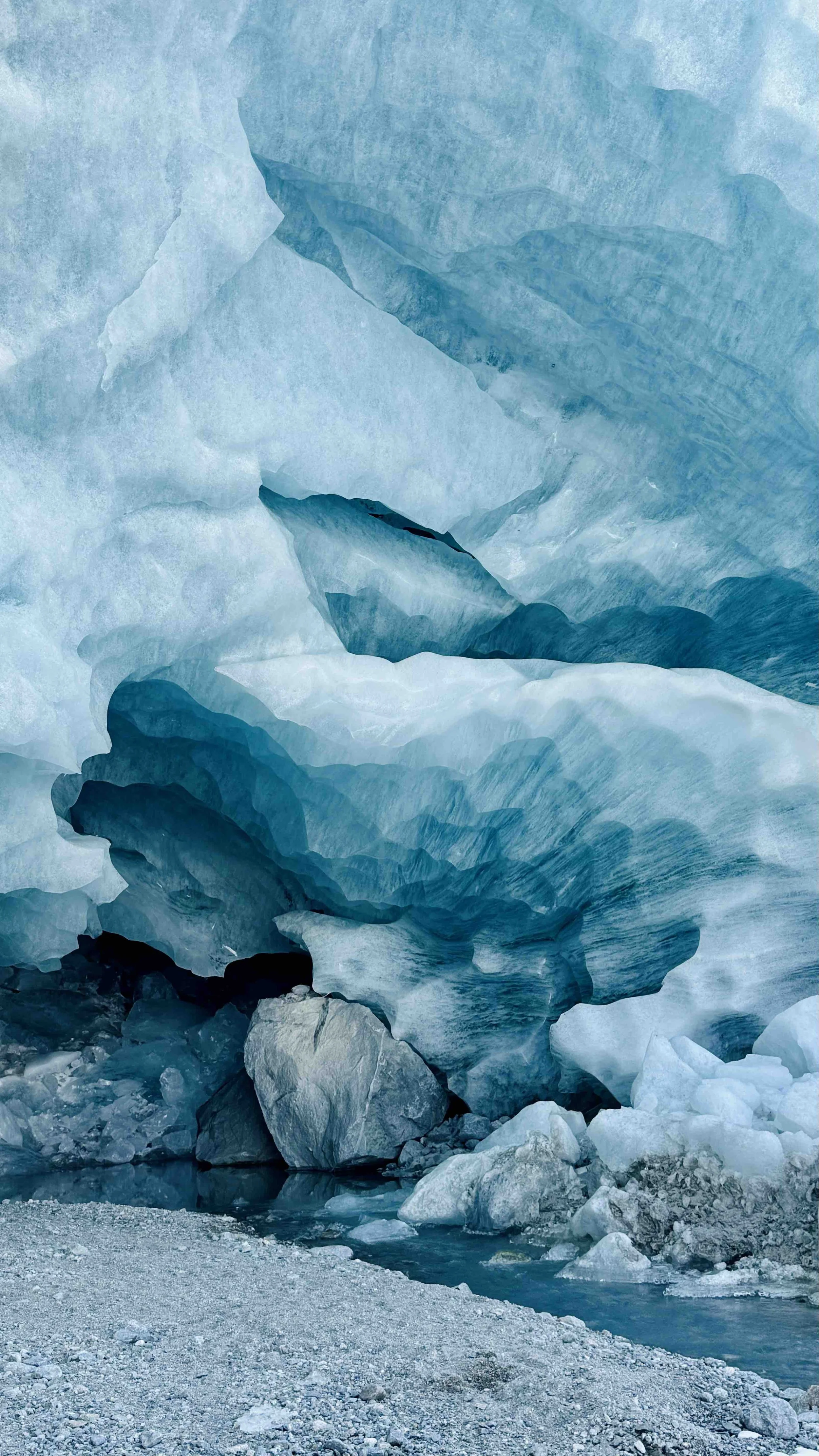 Close-up of a glacier with blue ice and rocks at the base, showing crevasses and ice formations.