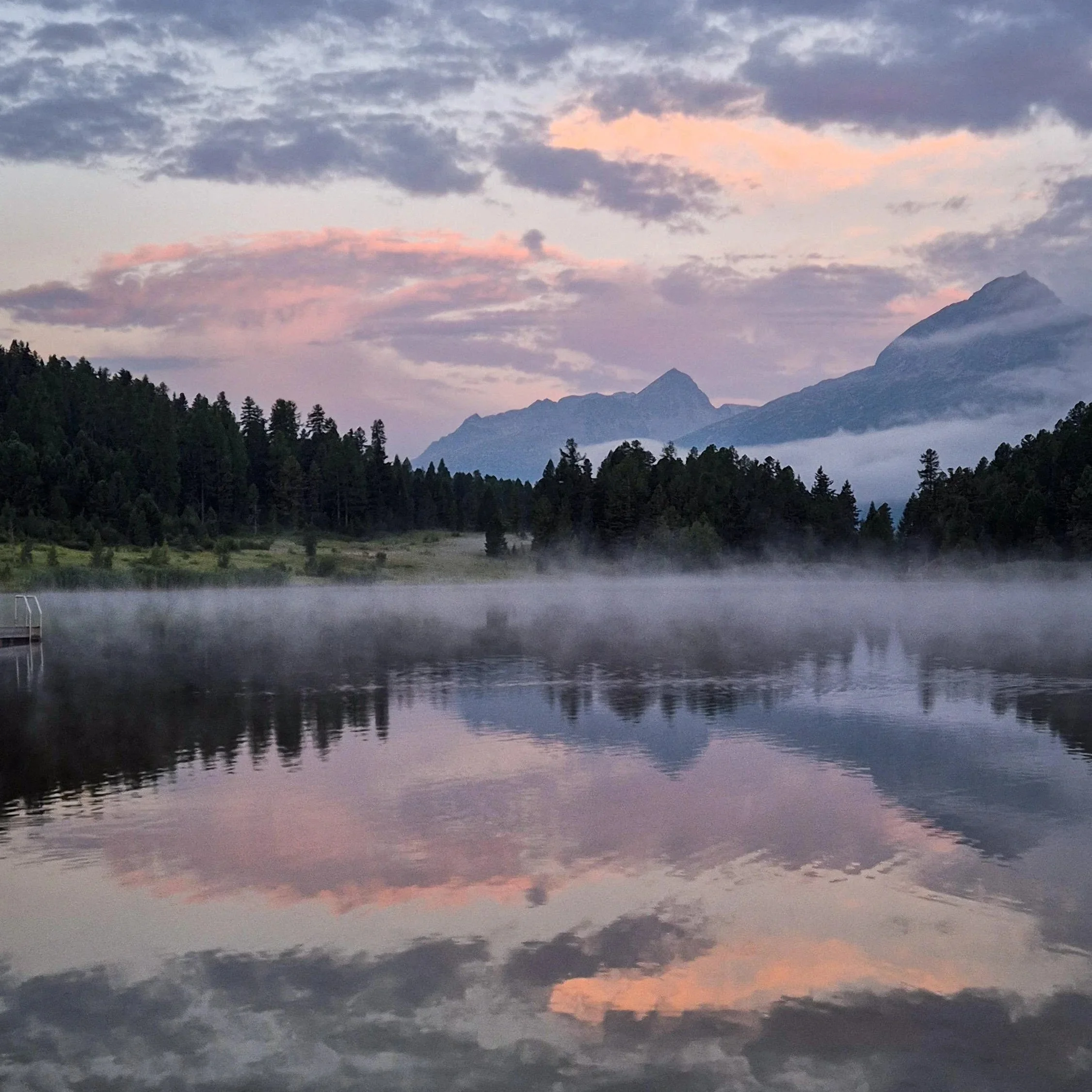 Scenic view of mountains under a cloudy sky at sunset, with a calm lake in the foreground reflecting the landscape.