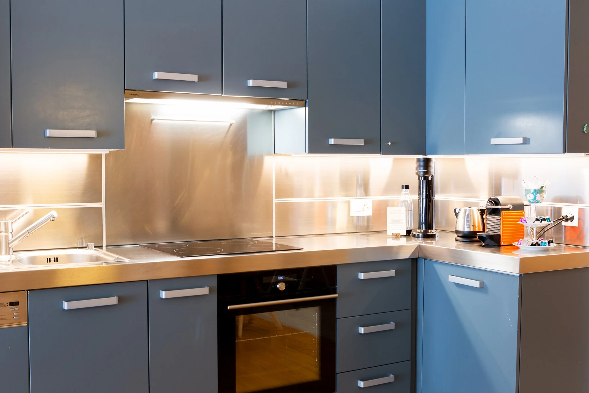 Modern kitchen with blue cabinets, stainless steel countertop, and black appliances, including a stove and oven.