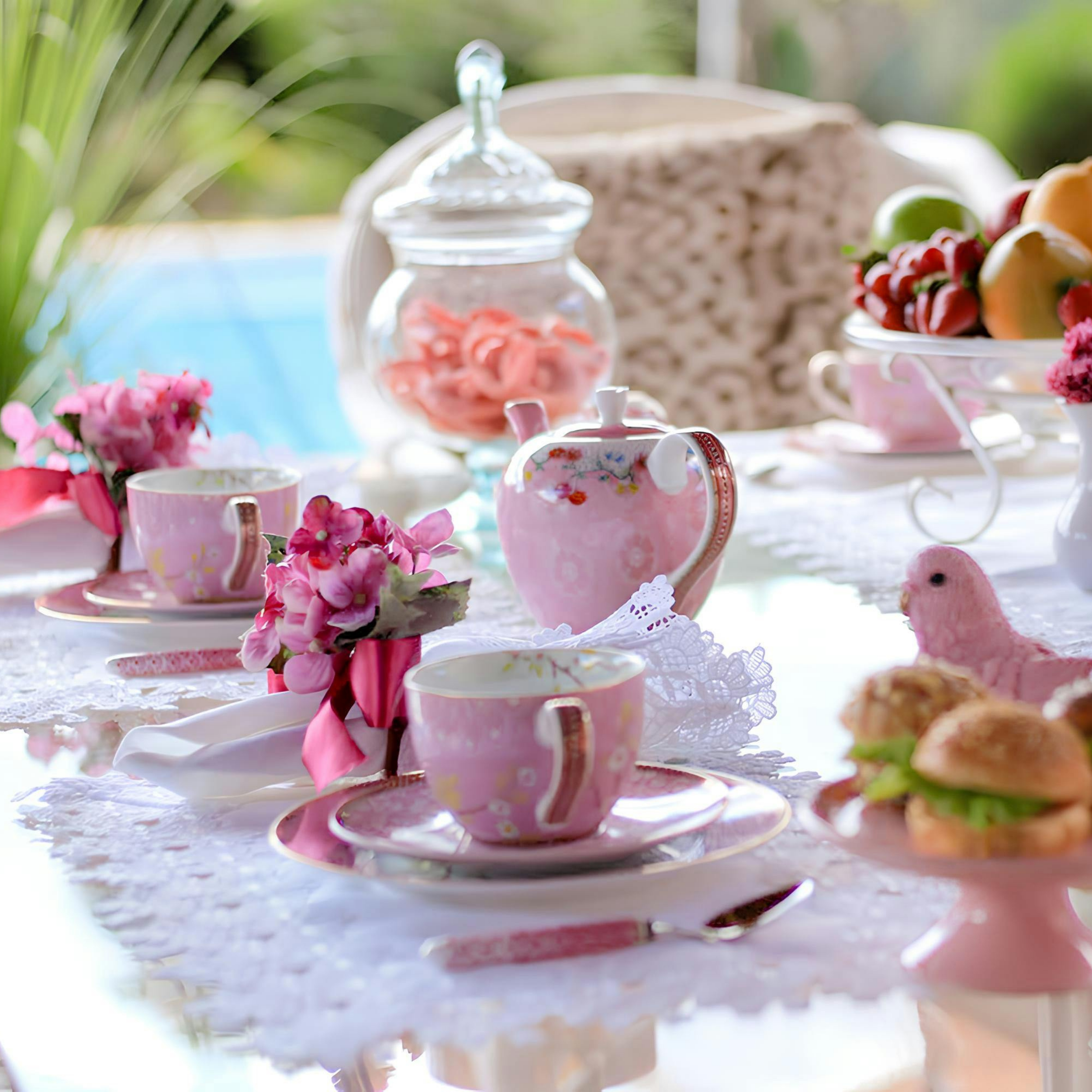 A visually blurred table setup with pink and white cups, a glass jar with pink candies, and a floral centerpiece, indicating a festive or celebratory occasion.