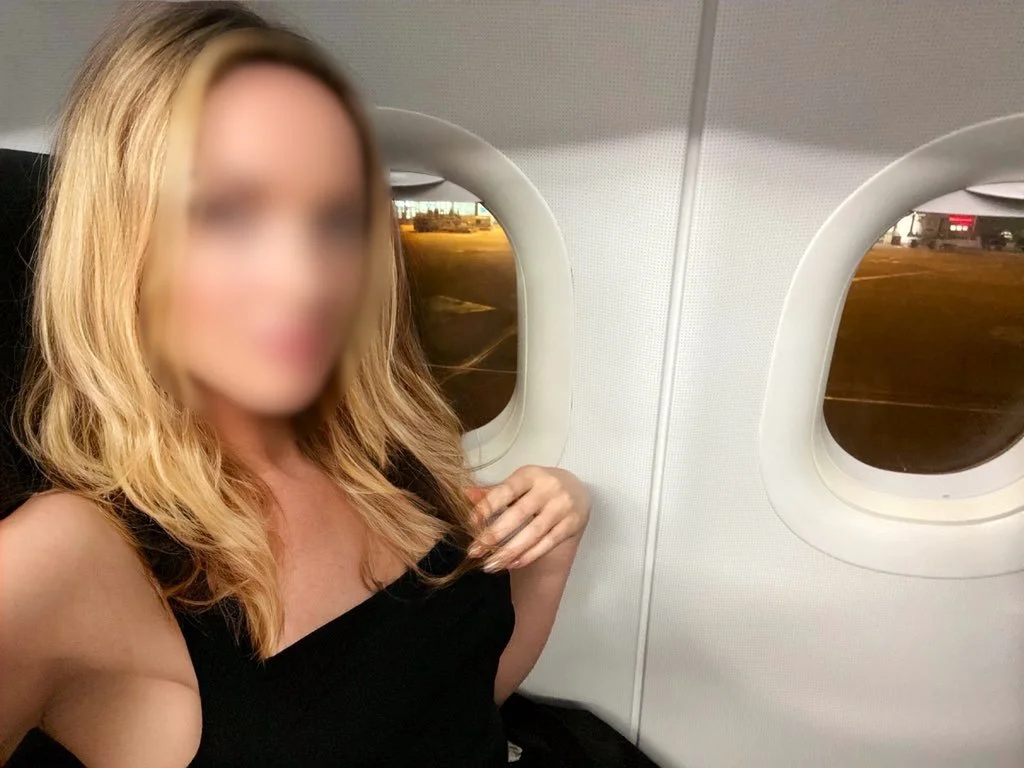Blonde high class independent London escort sitting in Business Class on an airplane, on a FMTY travel companion date.