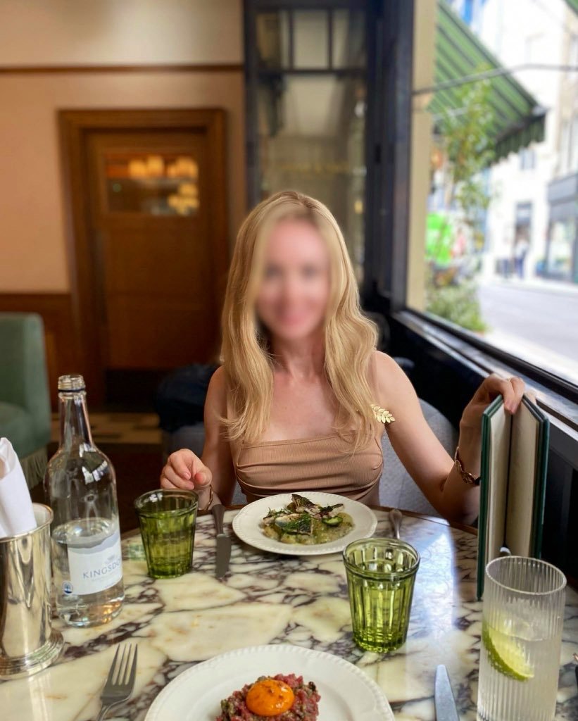 A blonde high class independent London escort sitting at a classy Soho restaurant table on a lunch date.