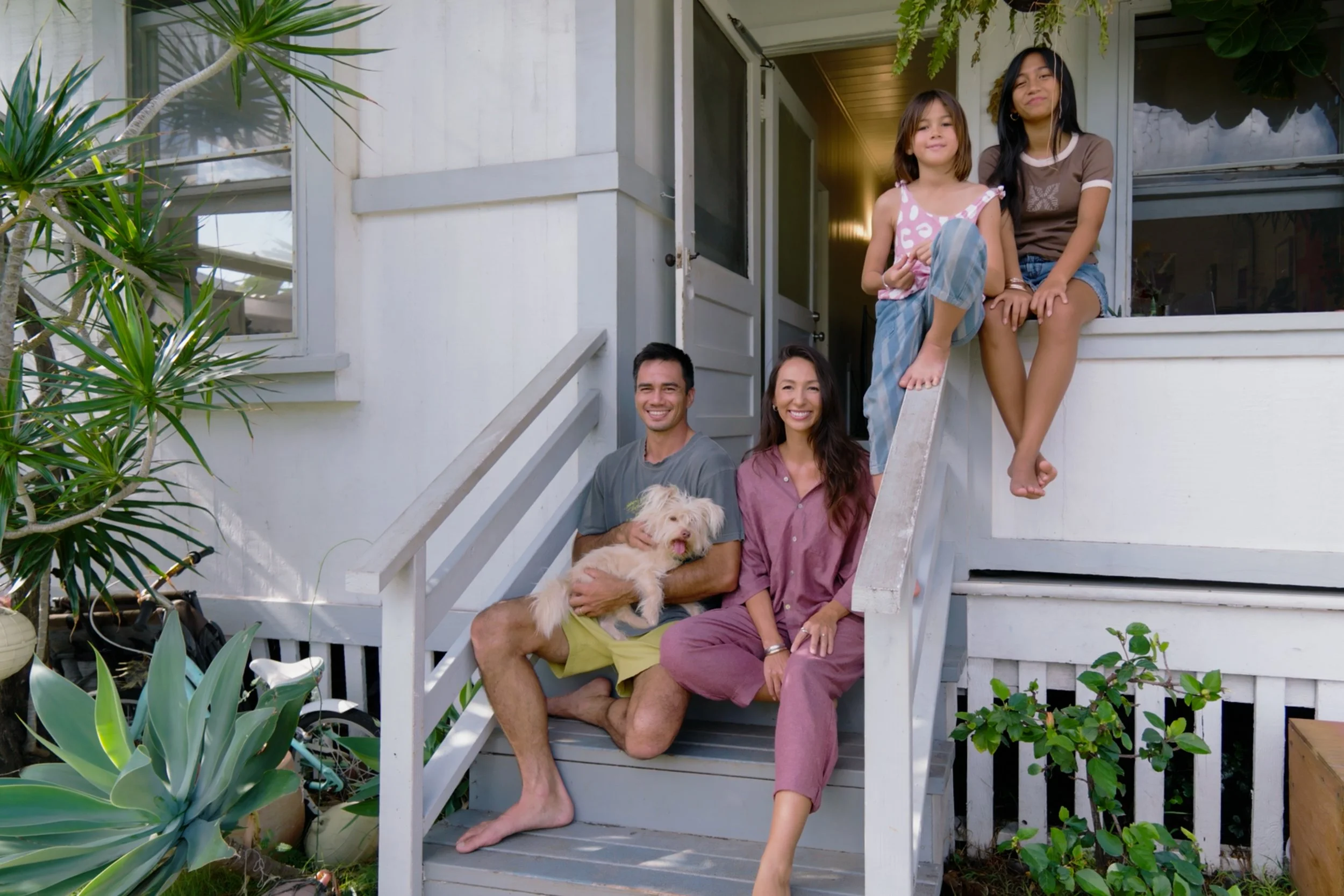 A family of five with a dog on the front porch of a house, smiling and posing for the photo.