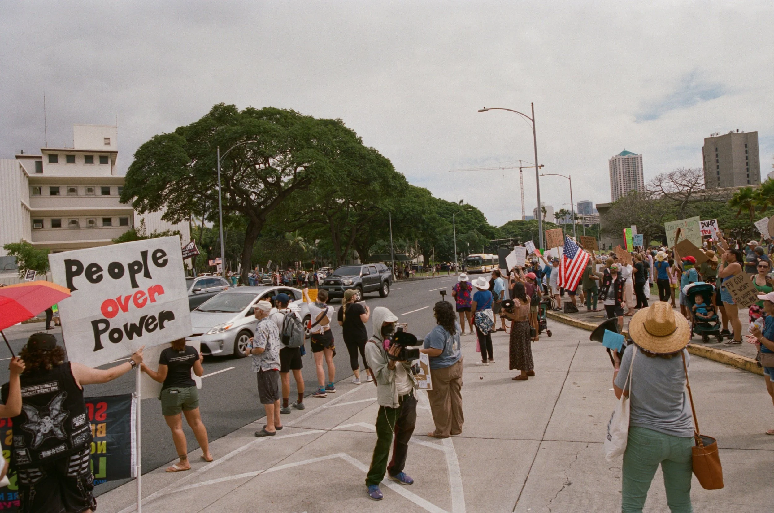 A diverse group of people participating in a protest on a city street, holding signs and American flags, with some individuals wearing hats and masks.